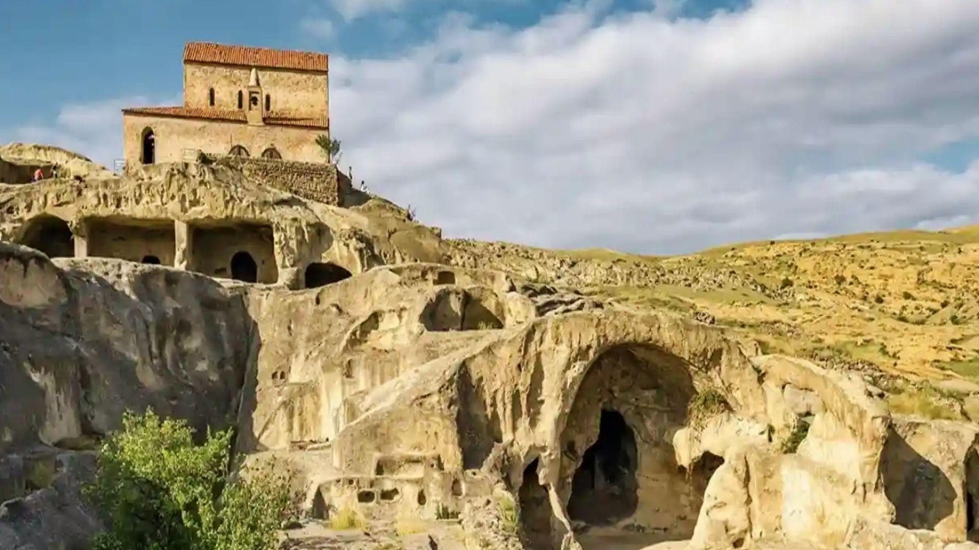 Ancient hilltop church and carved cave dwellings in rocky terrain, a historic landmark featured on cultural Savannah Plantation Tours.