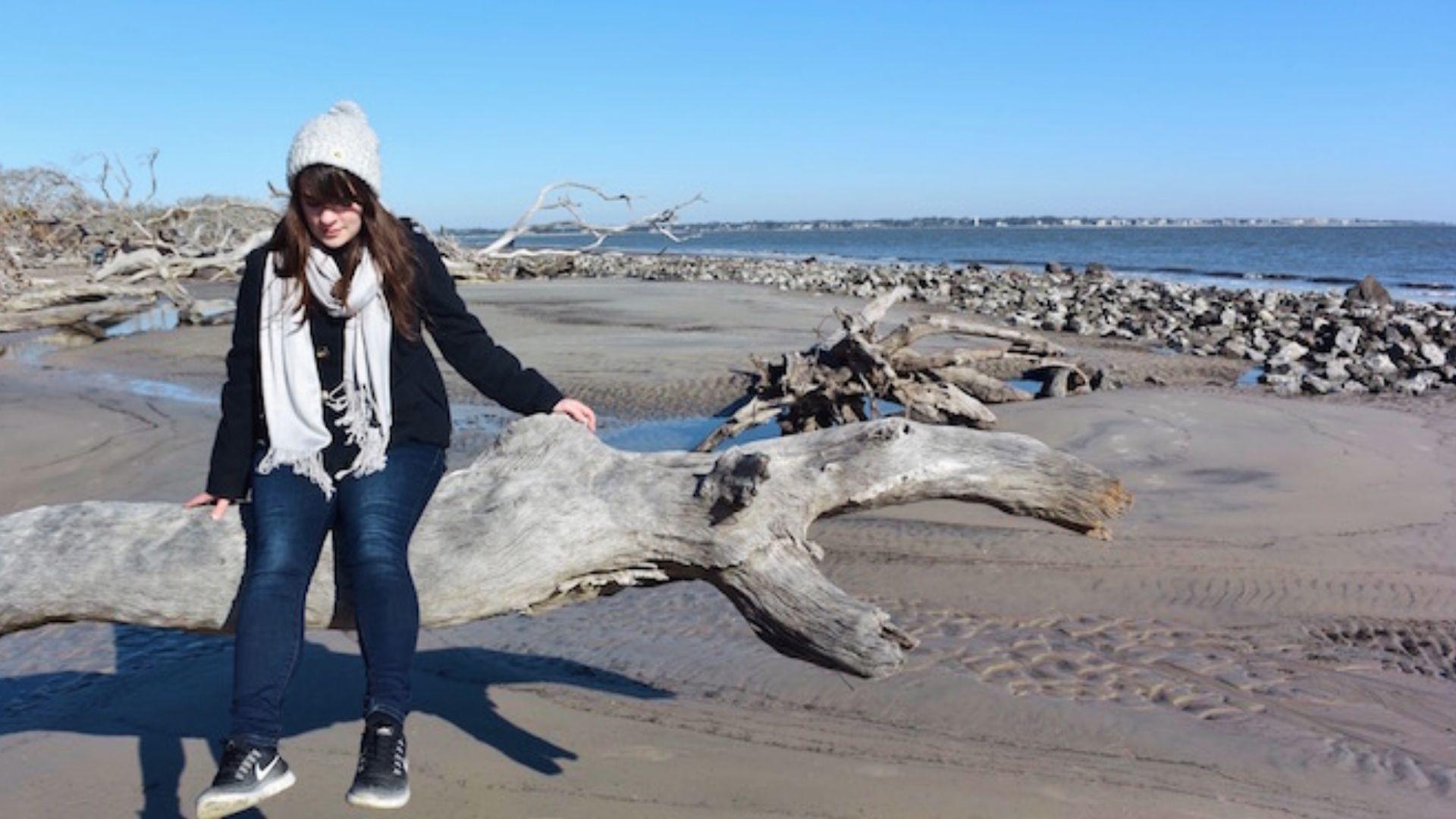 Woman in winter clothes sitting on driftwood at Jekyll Island Driftwood Beach near Savannah Georgia