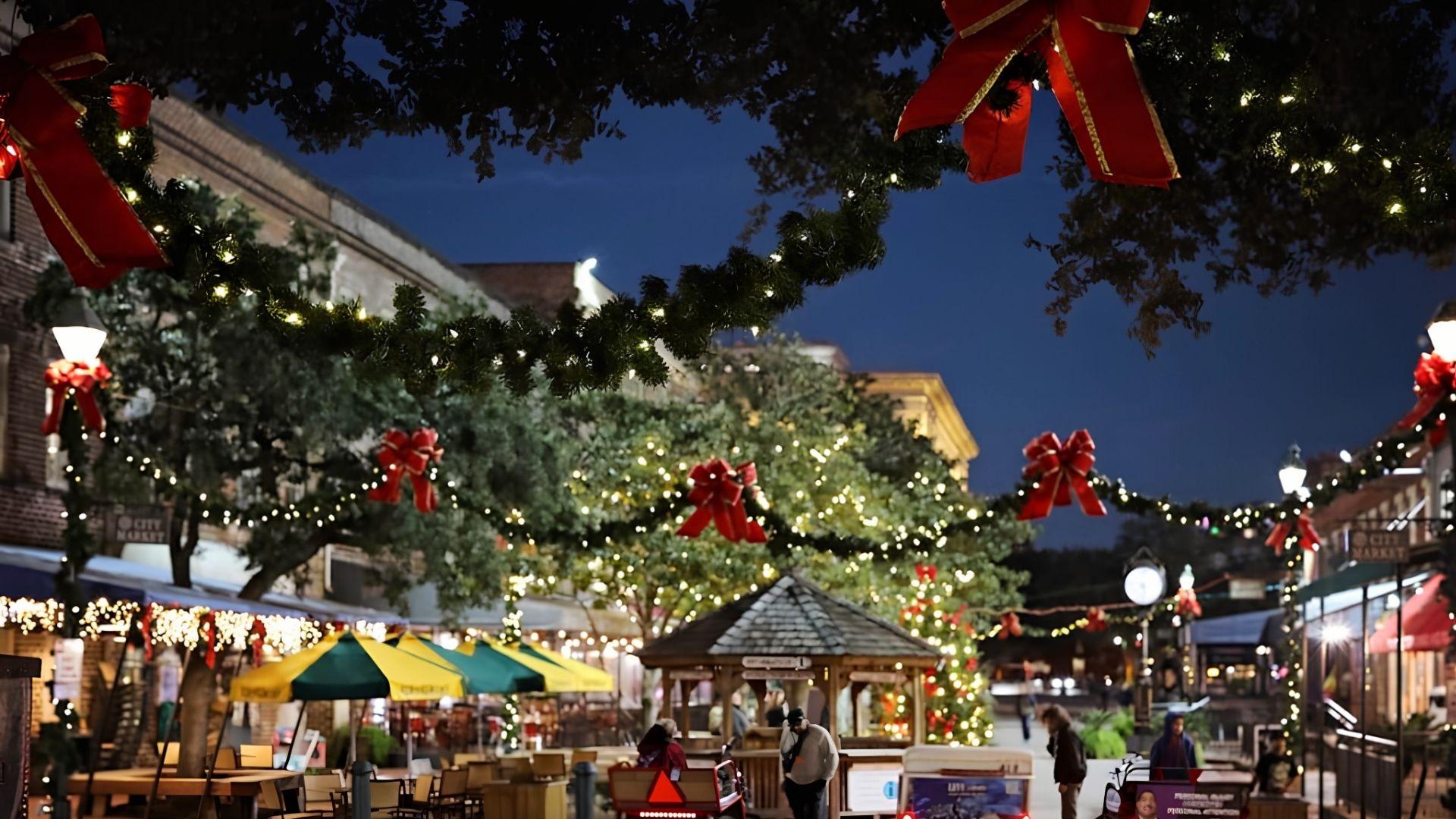 Savannah City Market plaza at night featuring overhead garlands, red bows, string lights, and Christmas trees by restaurants