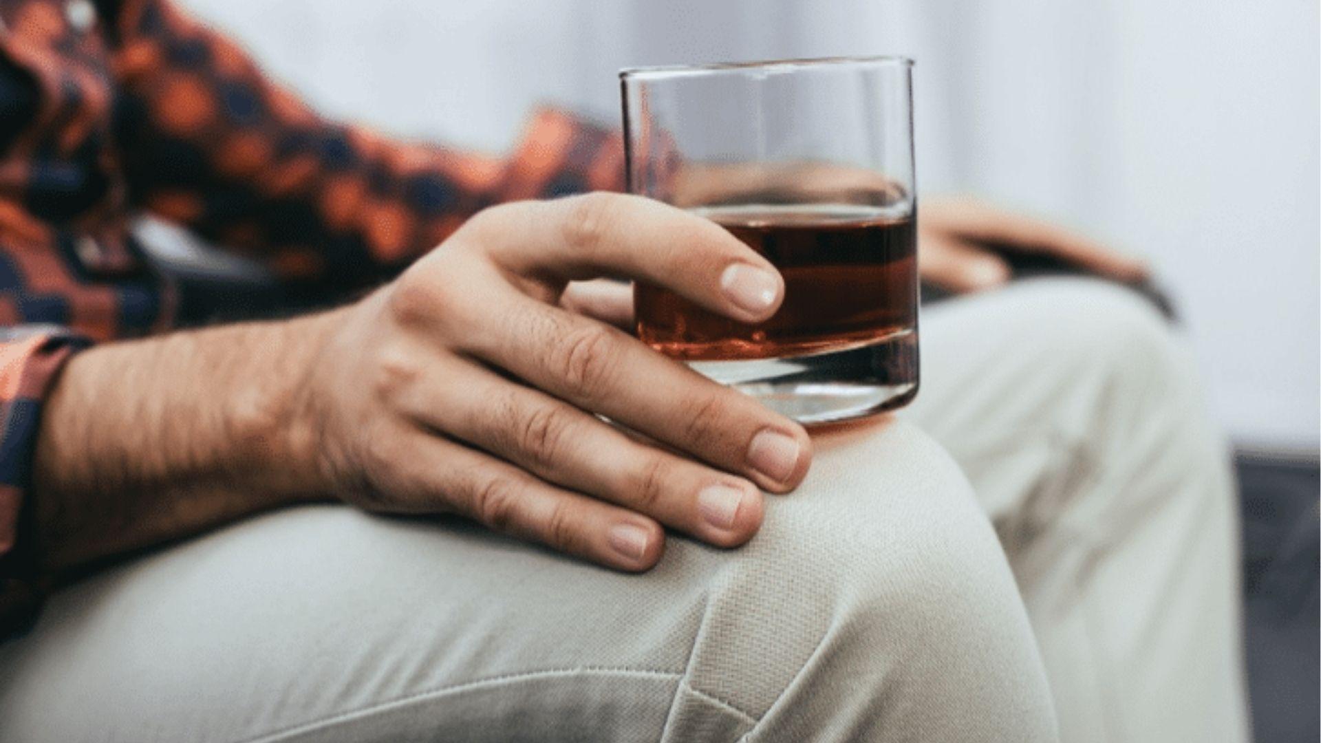 A person holding whiskey glass while seated, illustrating alcohol use before driving in Georgia is illegal.