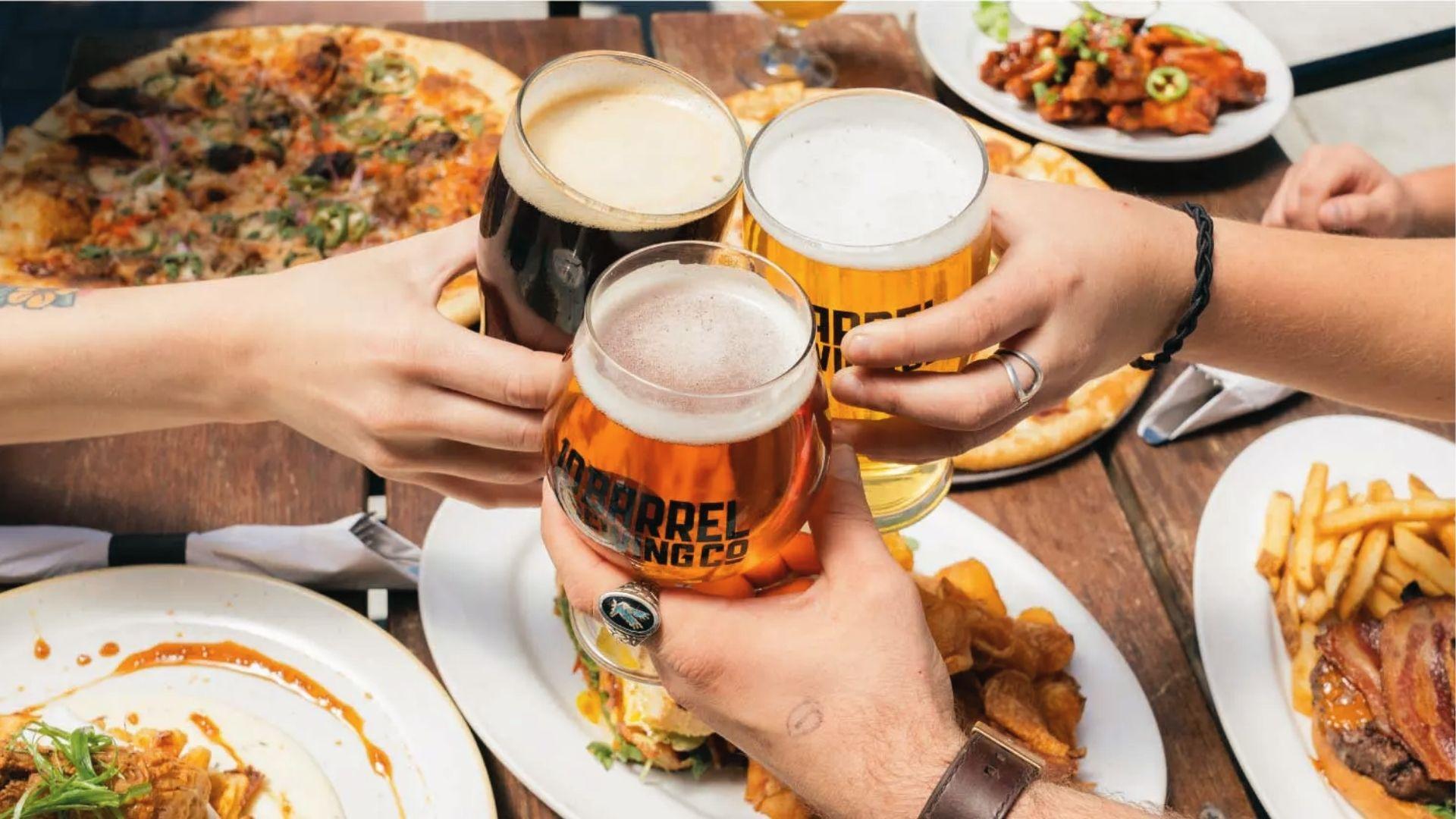 Friends clinking beer glasses over food, reminding that Georgia's legal BAC limit is 0.08 for drivers.