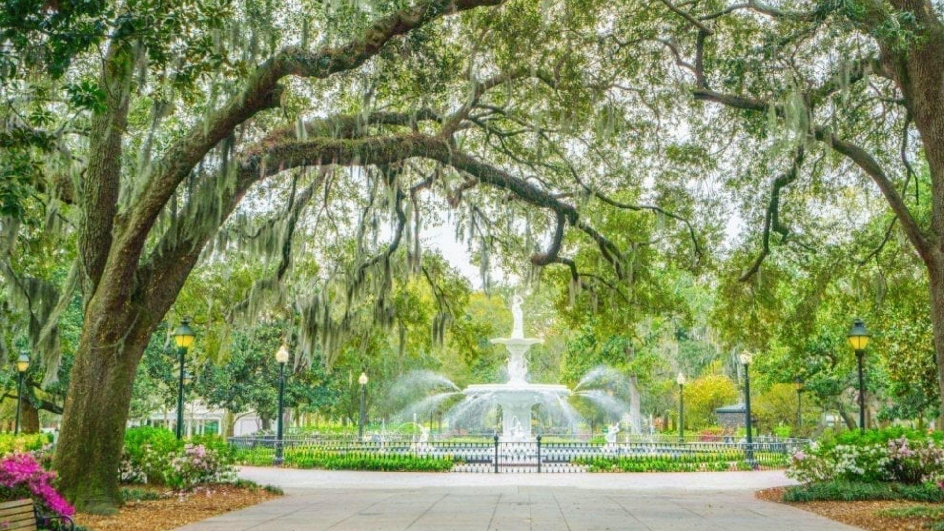 Forsyth Park fountain in Savannah framed by mossy oak trees and pink flowers, a scenic stop on historic Savannah Plantation Tours.