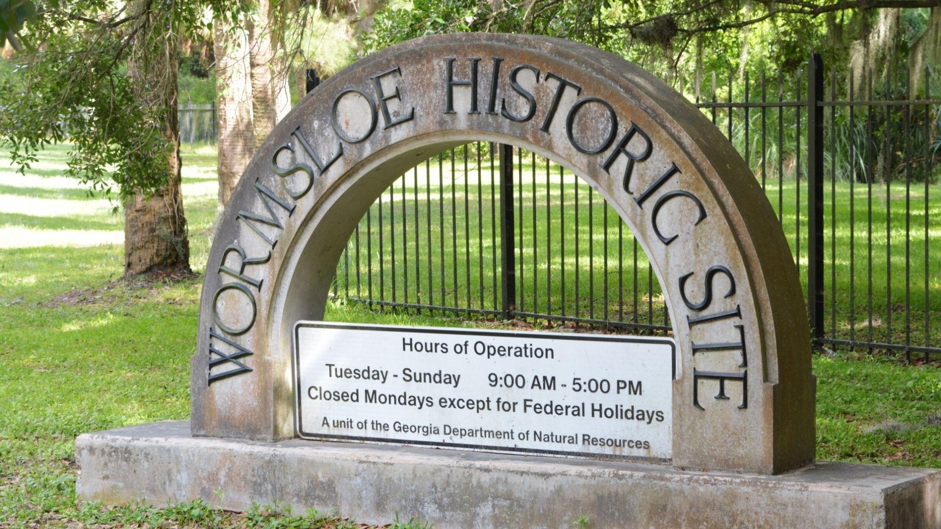 Wormsloe Historic Site stone arch entrance sign with hours of operation, marking a key colonial plantation stop on Savannah Plantation Tours.