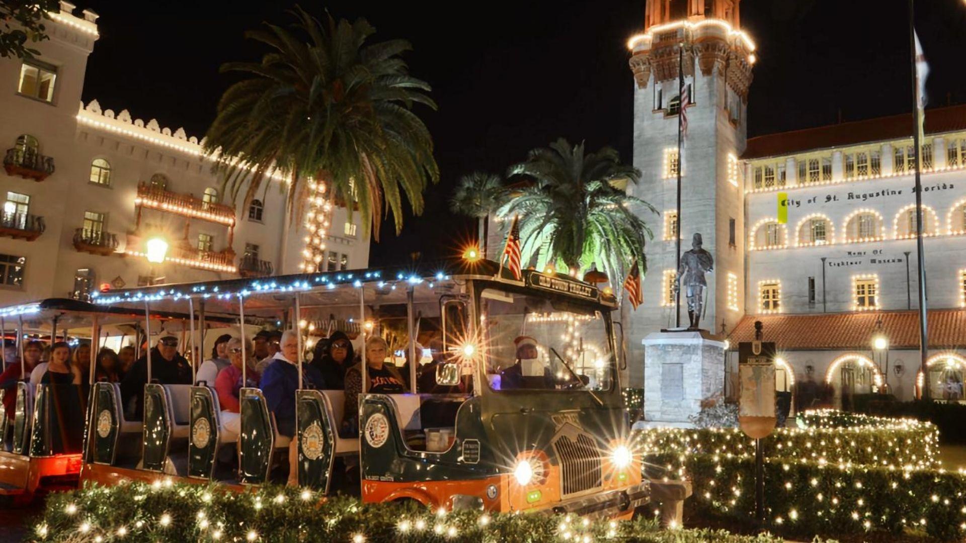 Christmas trolley tour passing Lightner Museum in St. Augustine with white holiday lights, palm trees, and festive nighttime decor
