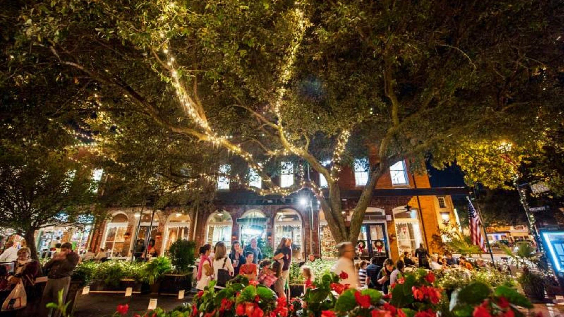 City Market in Savannah at night with oak trees wrapped in Christmas lights, red bows, and festive outdoor dining