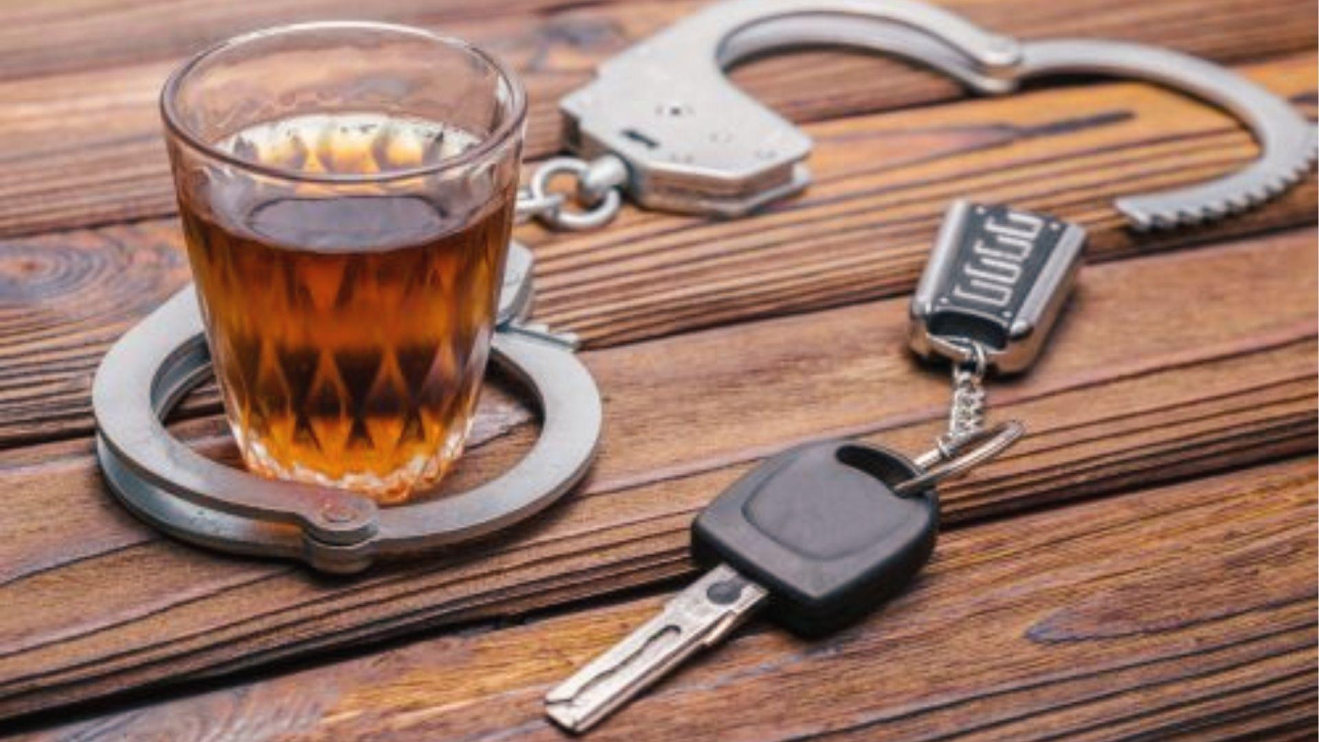 Whiskey glass, handcuffs, and car keys on wood, showing DUI penalties if over Georgia's BAC limit.