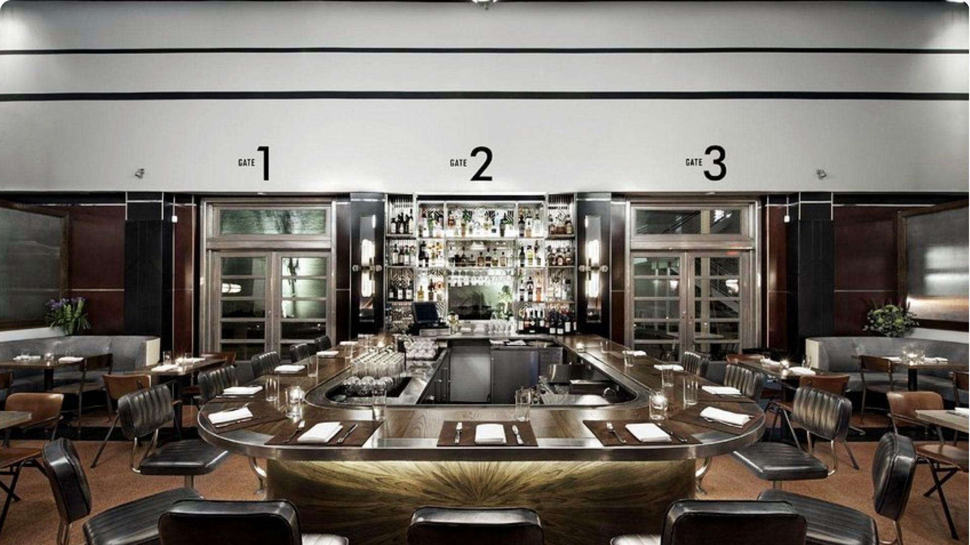 Sleek, upscale Art Deco–style bar and dining room with a horseshoe-shaped dark wood bar, leather seating, and Gate 1, 2, 3 signage on the walls.