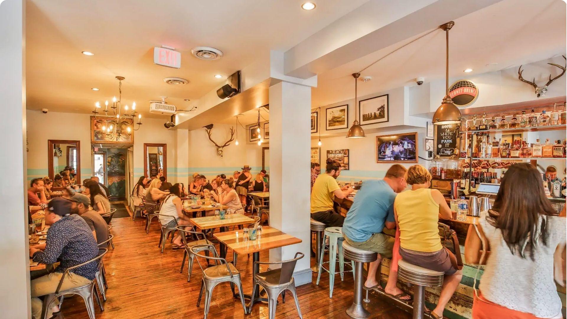 Lively, warmly lit casual restaurant interior packed with diners at wooden tables and bar stools, with antler décor and a well-stocked bar.