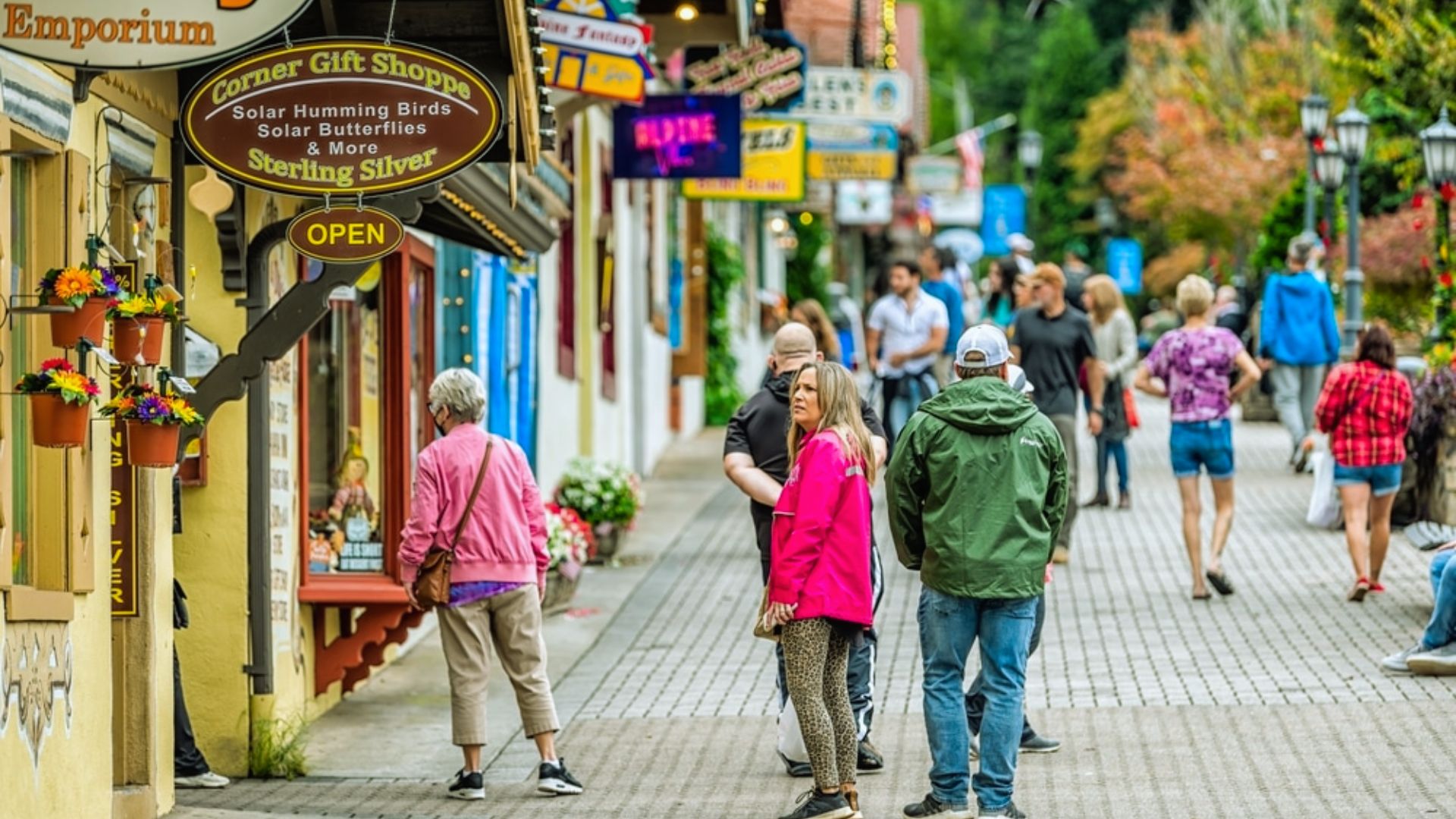 "Tourists walk a brick shopping street lined with gift shops and flower baskets on an autumn day."