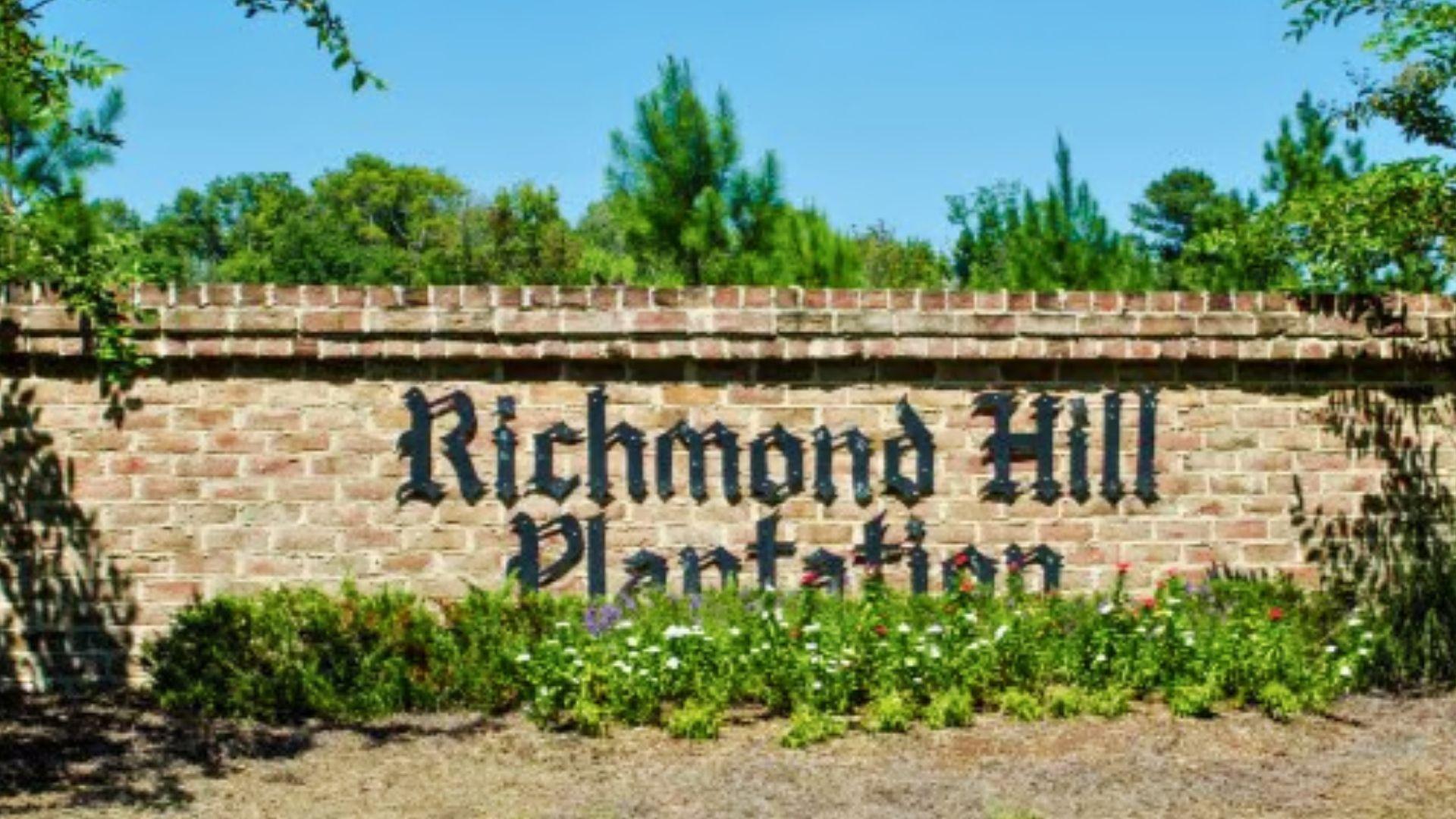 Richmond Hill Plantation entrance sign on brick wall with flowers and pines, welcoming visitors to historic Savannah Plantation Tours sites.