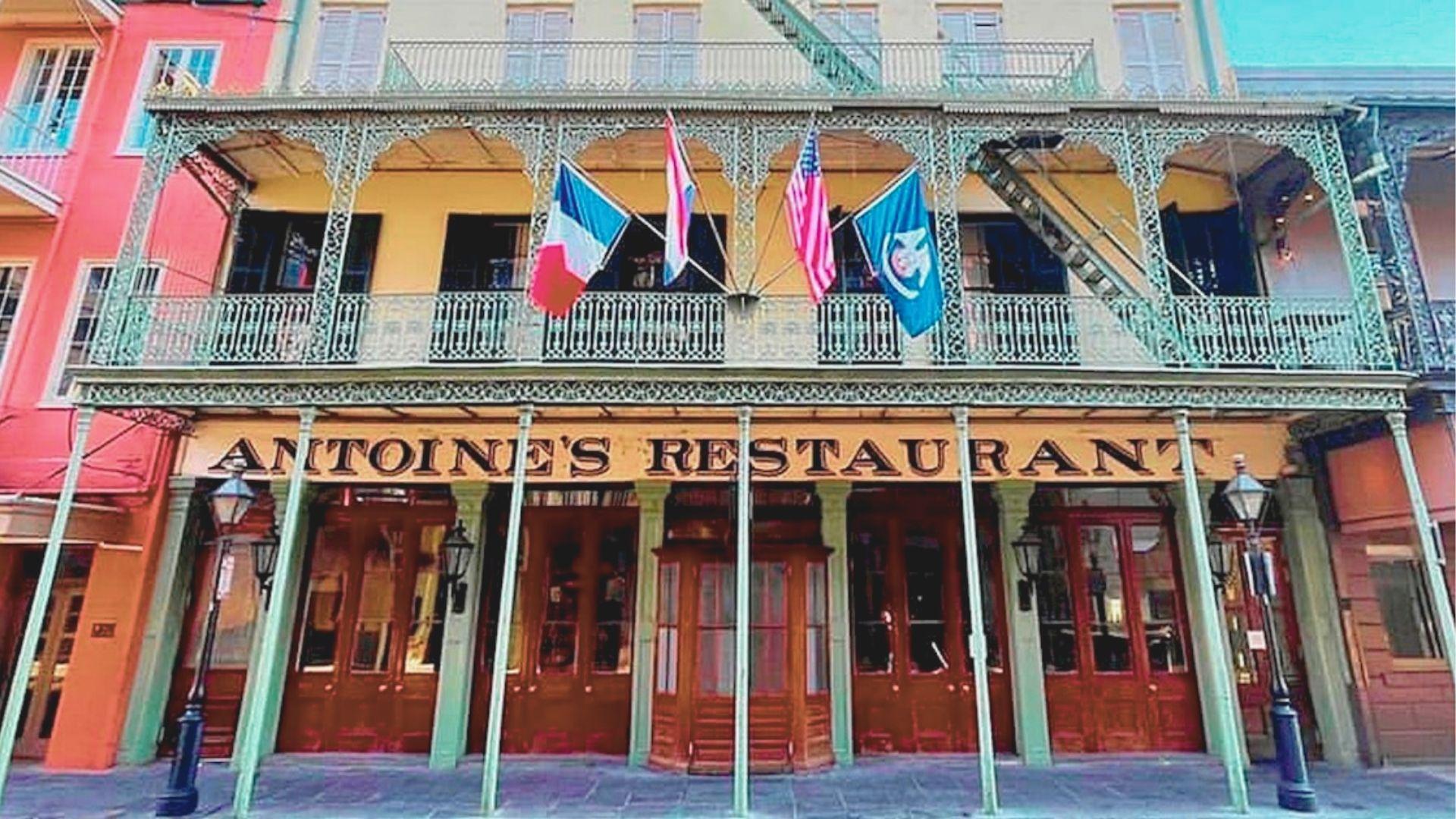 Historic Antoine's Restaurant facade in the French Quarter with ornate iron balconies and French, US, and Louisiana flags.