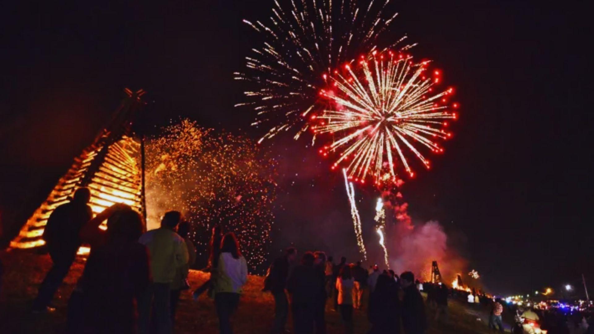 Christmas Eve bonfires and fireworks over Mississippi River levee with silhouetted crowd watching, sparks lighting night sky