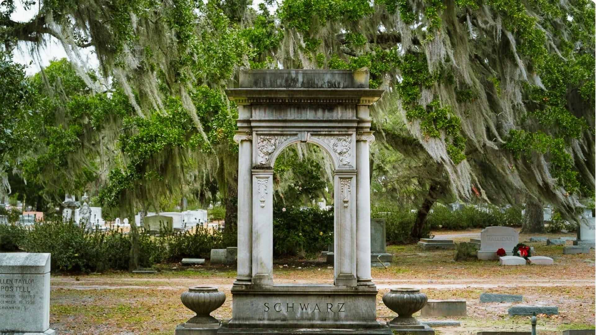 A weathered tombstone surrounded by trees and moss in Bonaventure Cemetery, a serene atmosphere.