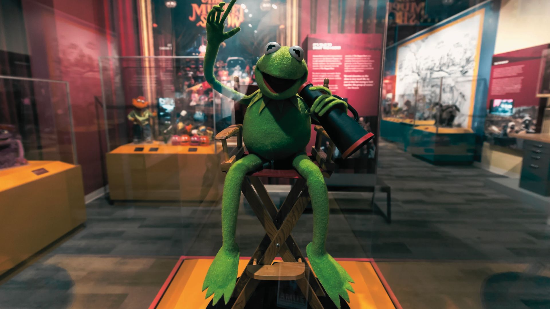 Kermit, the Frog display, seated in the director chair inside the colorful Center for Puppetry Arts exhibit.