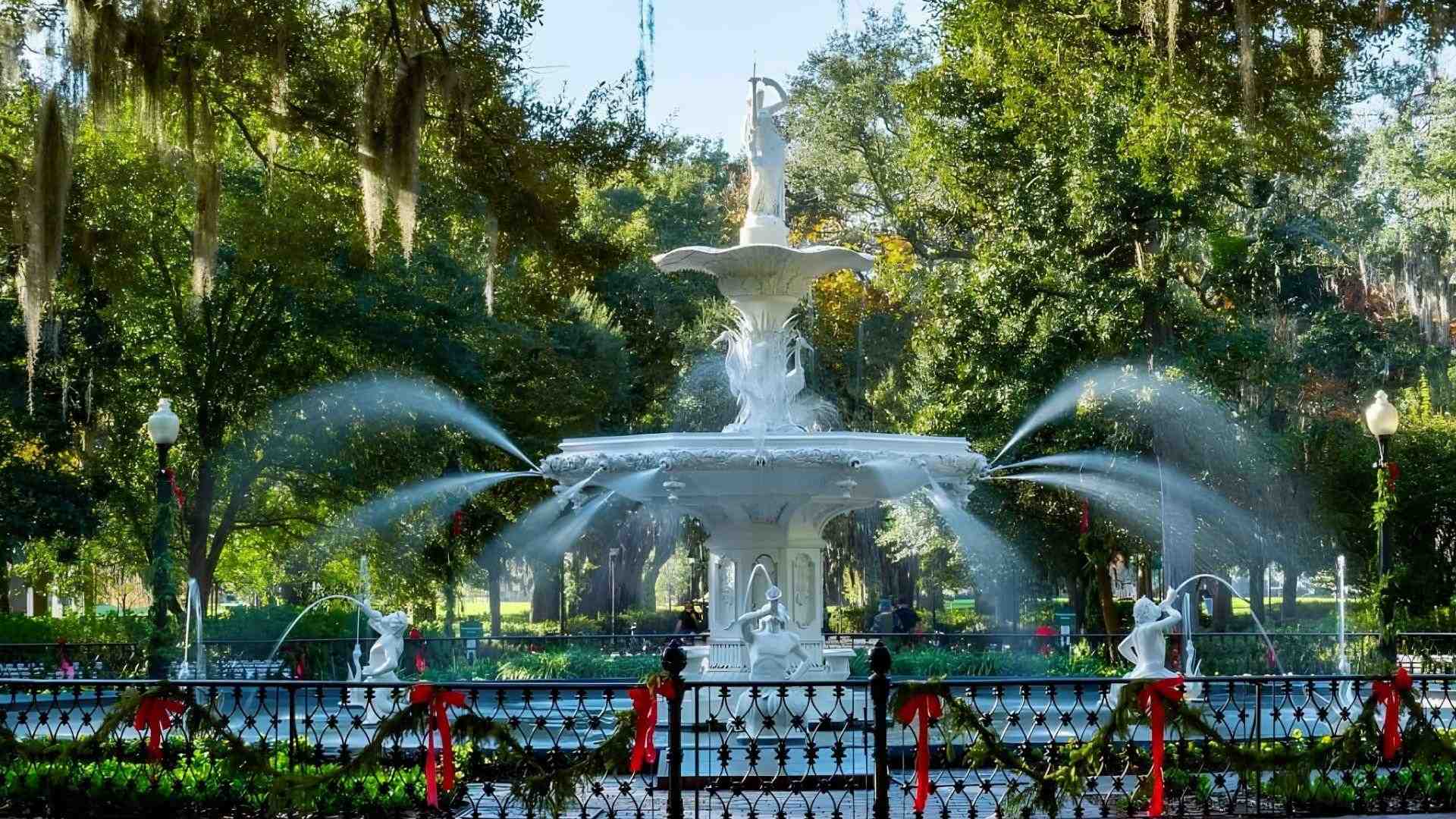 Forsyth Park fountain in Savannah decorated with holiday garlands and red bows, spraying water under Spanish moss trees