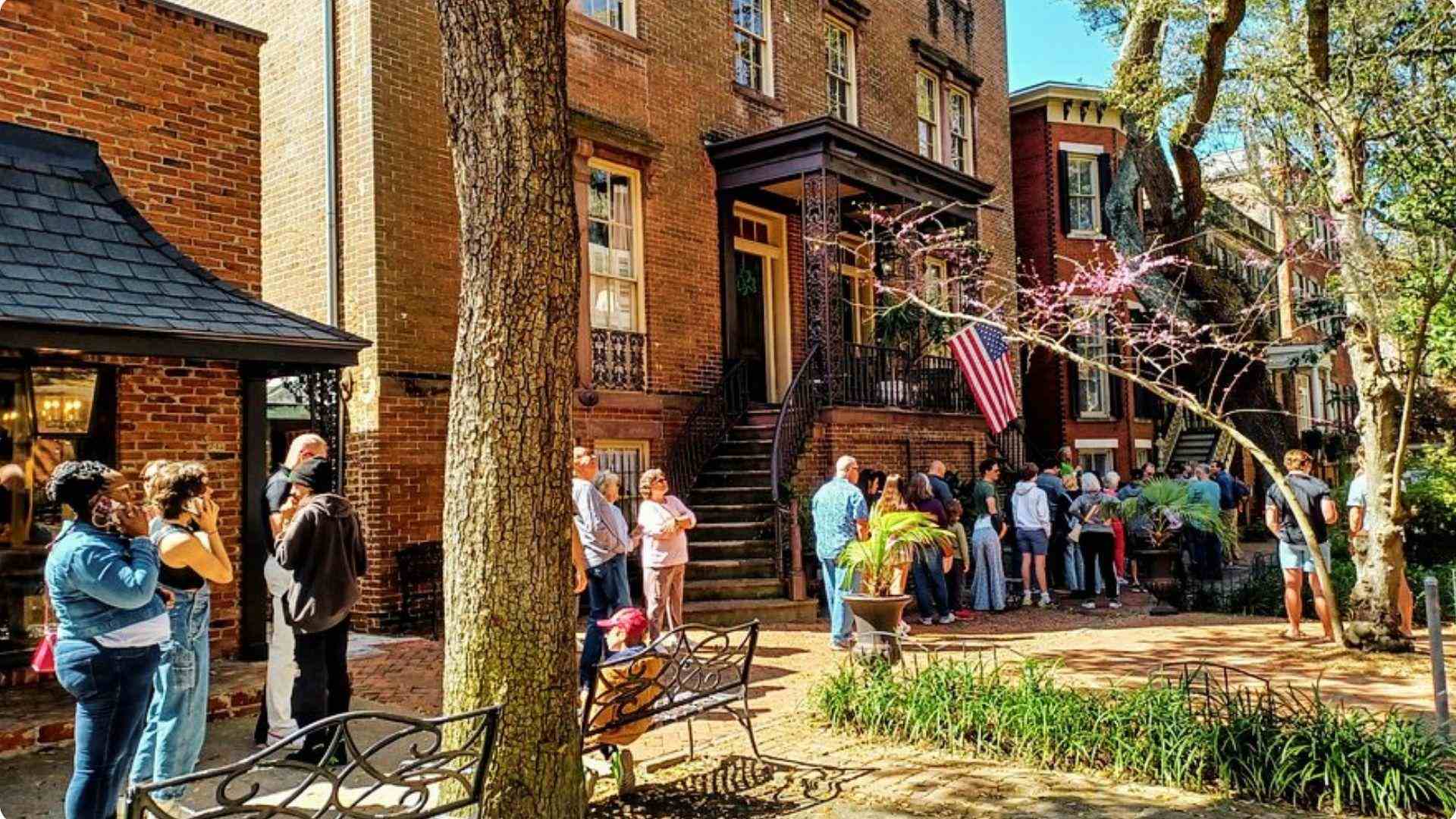 Daytime crowd of guests lining up outside a historic three-story brown brick townhouse.