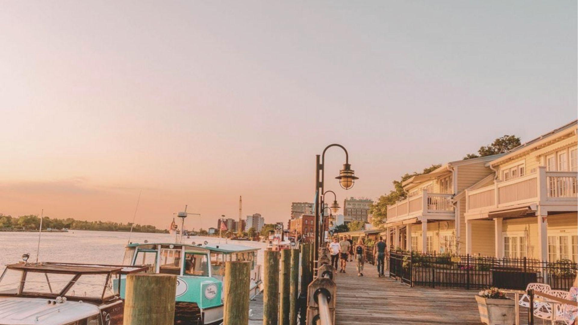 Golden hour lights up the Wilmington Riverwalk as boats dock along the Cape Fear River.