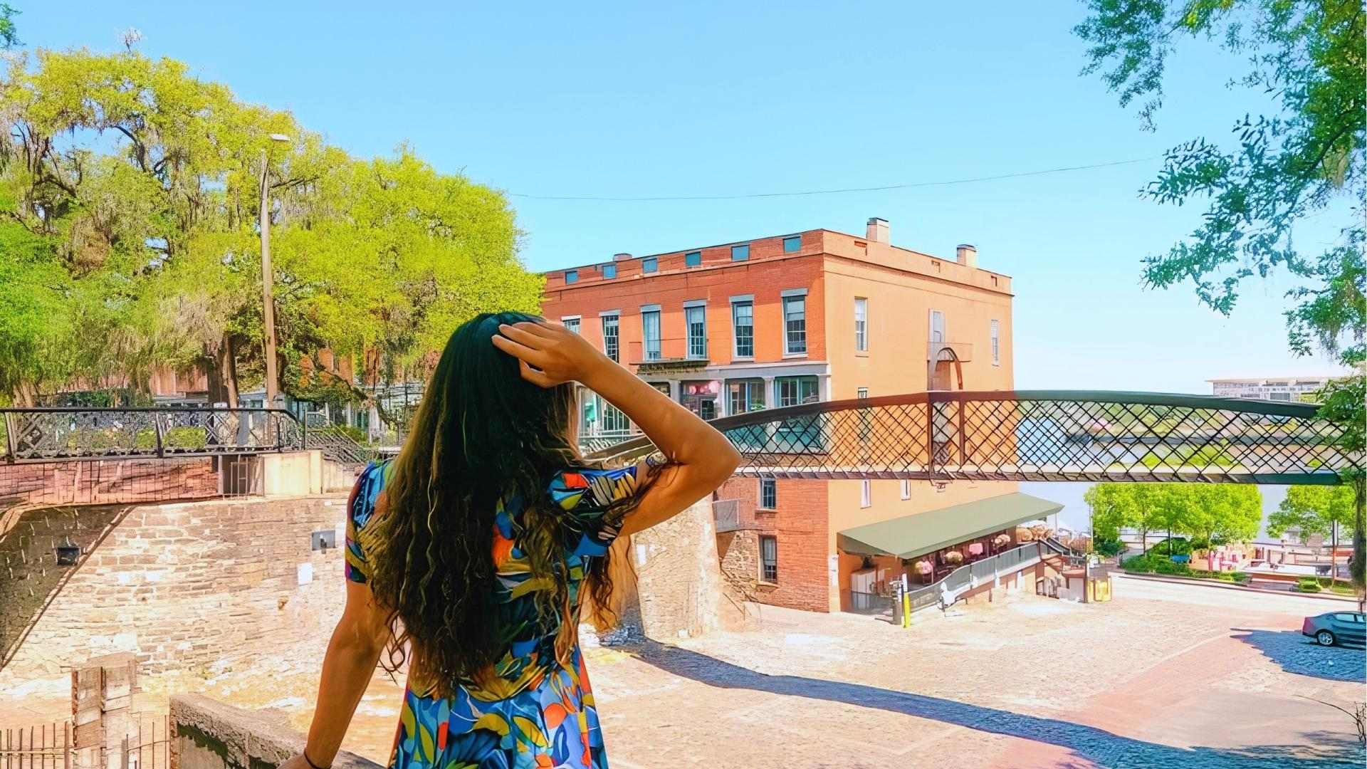 Woman in colorful dress overlooking Factors Walk pedestrian bridge and River Street Savannah.