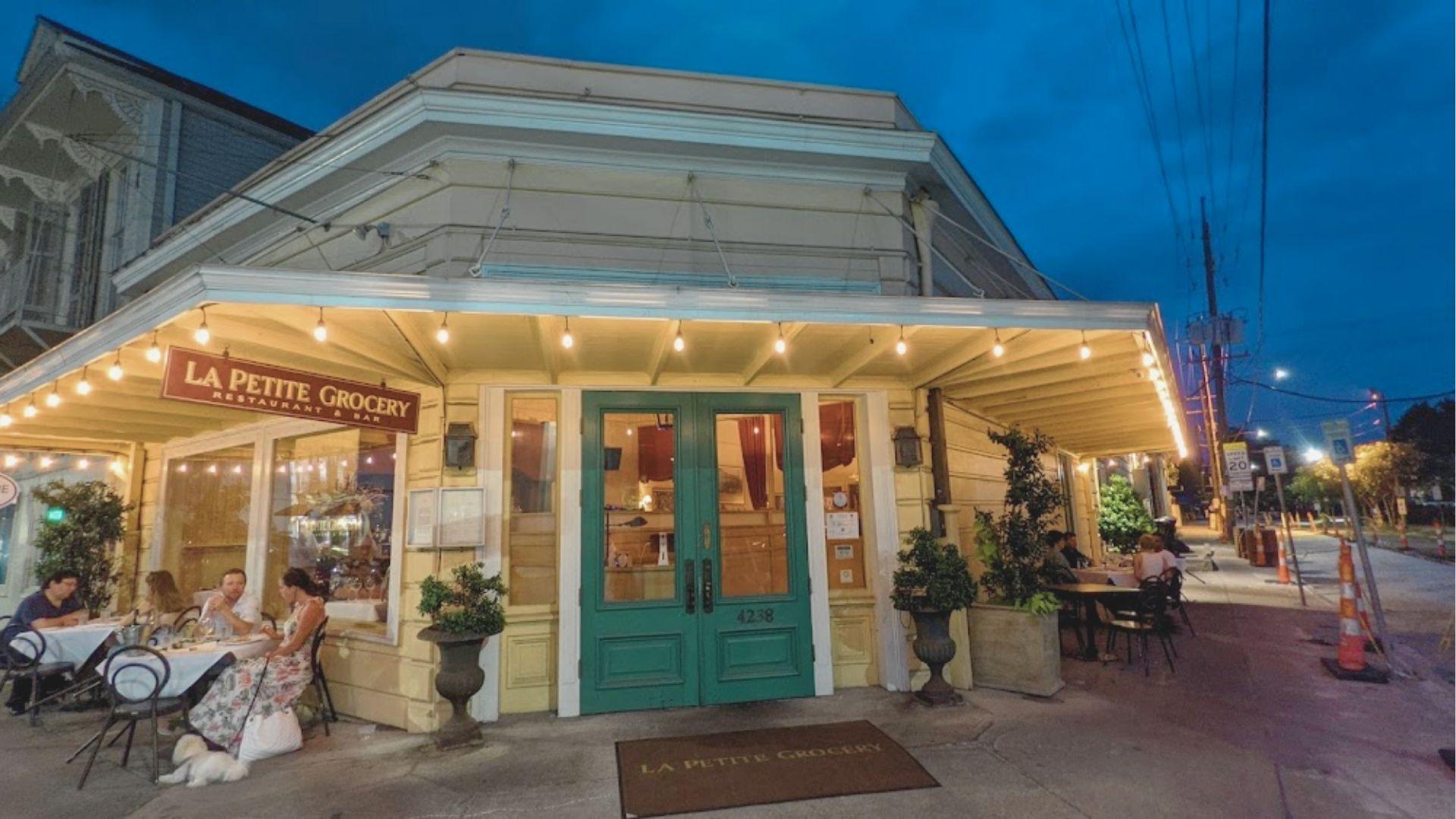 La Petite Grocery’s teal double doors and string-lit patio glow at dusk on a New Orleans street.