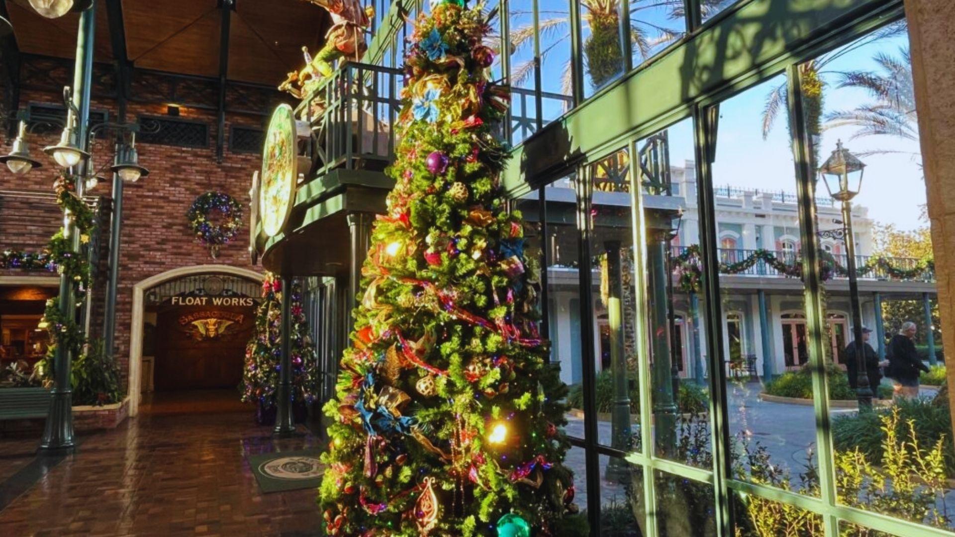 Sunlit indoor atrium with large decorated Christmas tree, wreaths, garland, brick walls, Float Works entrance, glass windows