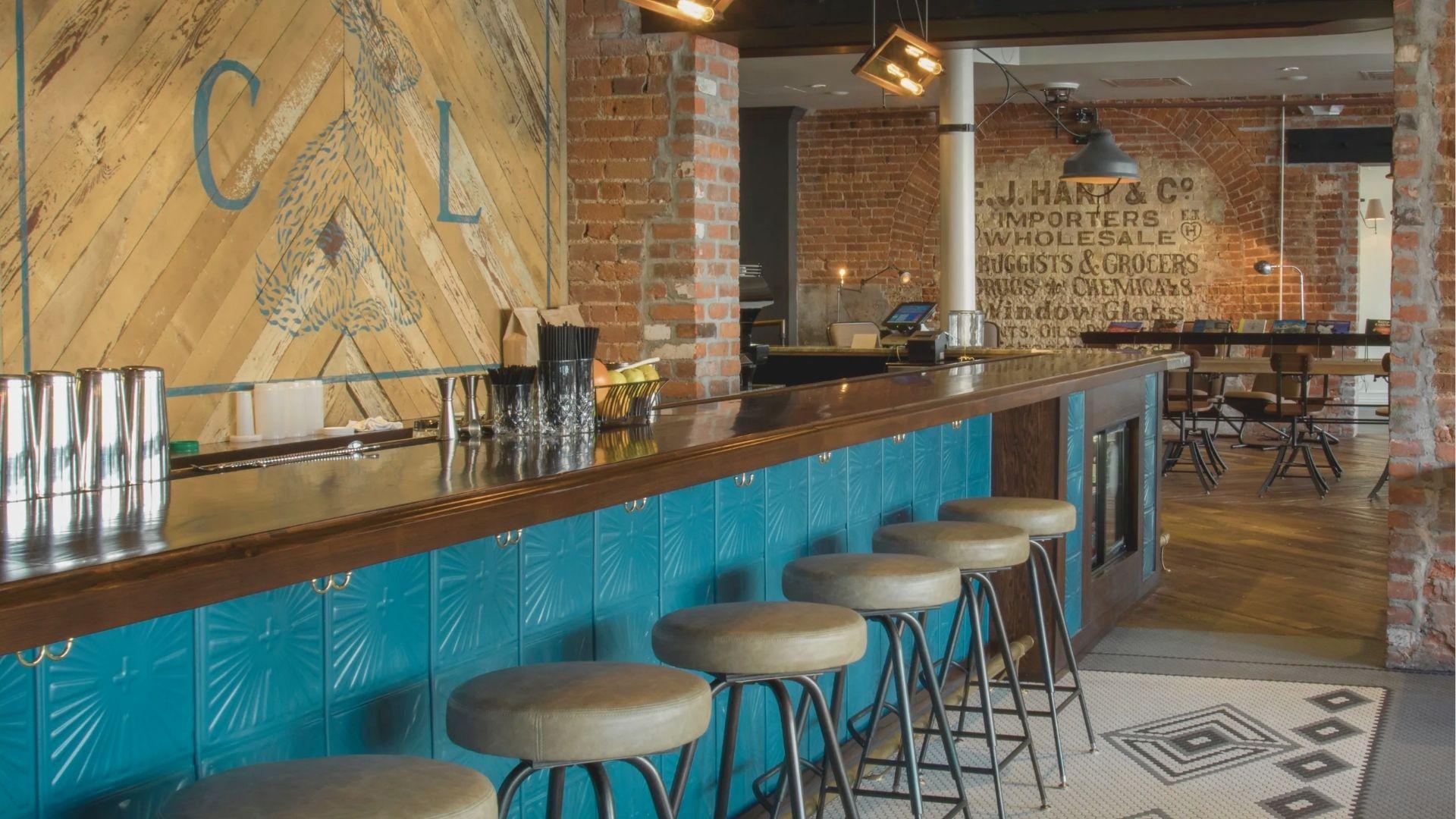 Industrial-chic bar with turquoise tile, exposed brick, and vintage “E.J. Hart & Co.” mural in New Orleans.