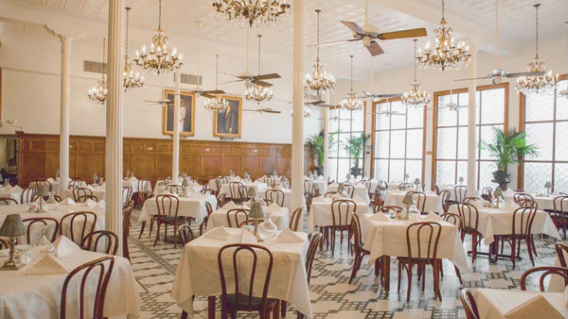 Classy dining room with white-clothed tables, bentwood chairs, crystal chandeliers, and black-and-white tile floors.