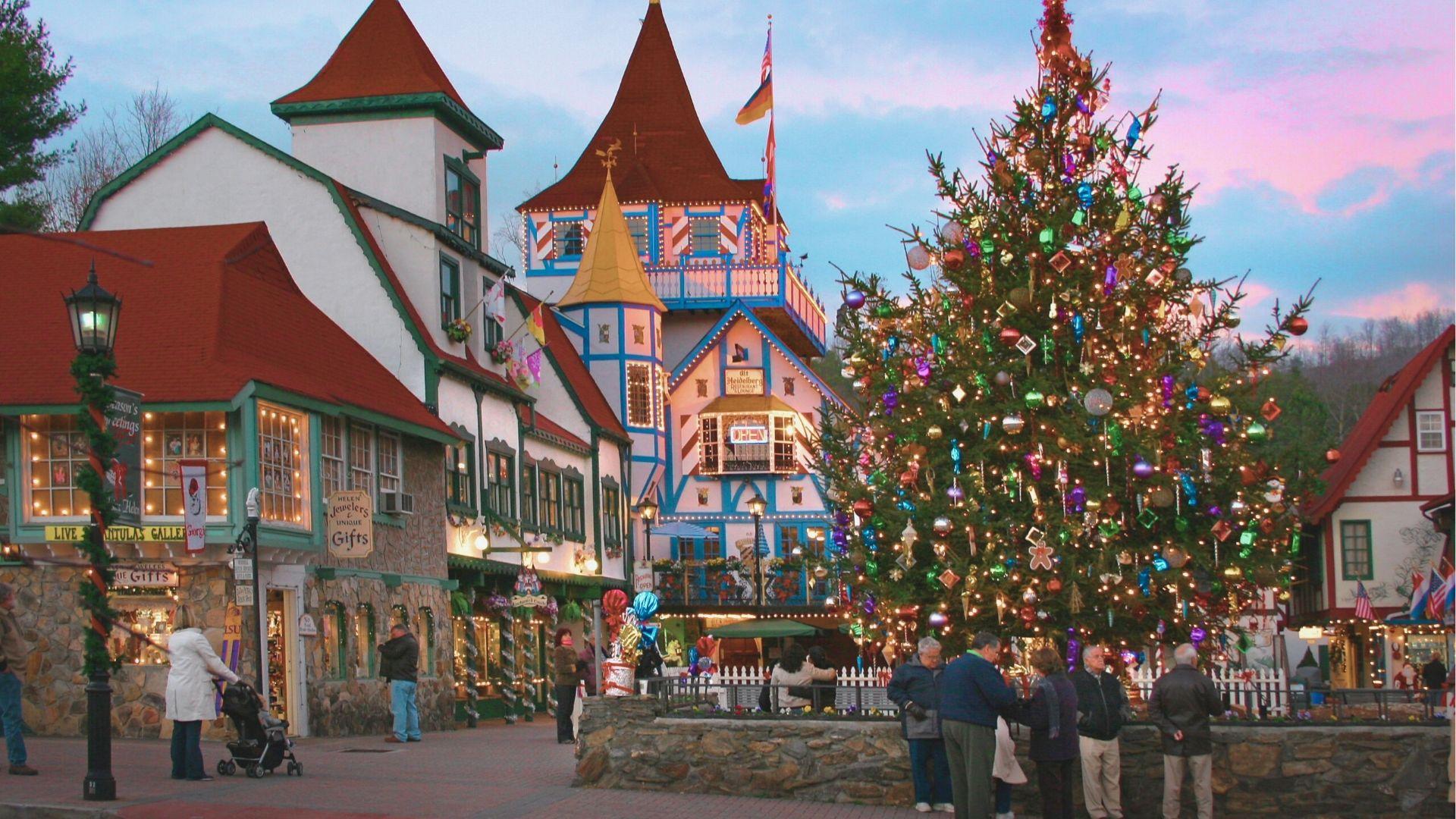 Bustling Helen town square at twilight with a massive ornament-covered Christmas tree beside colorful shops.