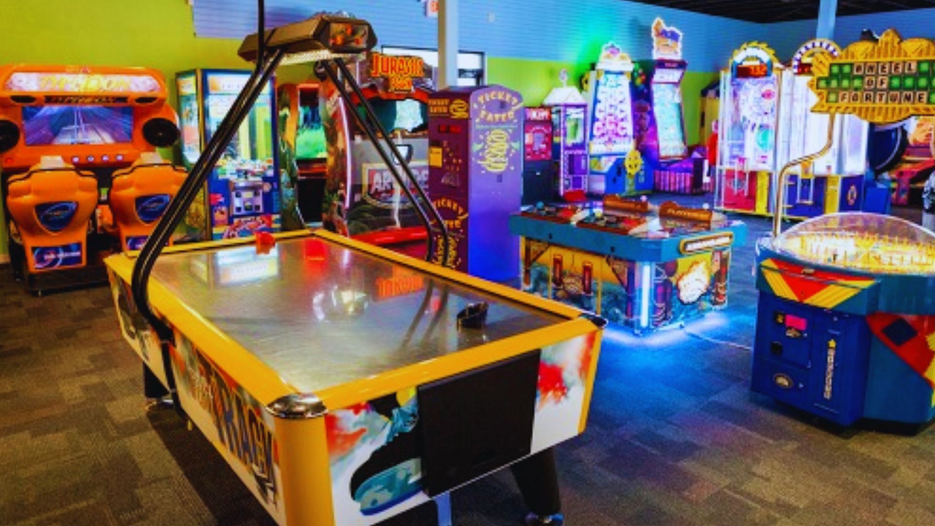 A colorful arcade room with an air hockey table and many game machines at Adventure Cove.