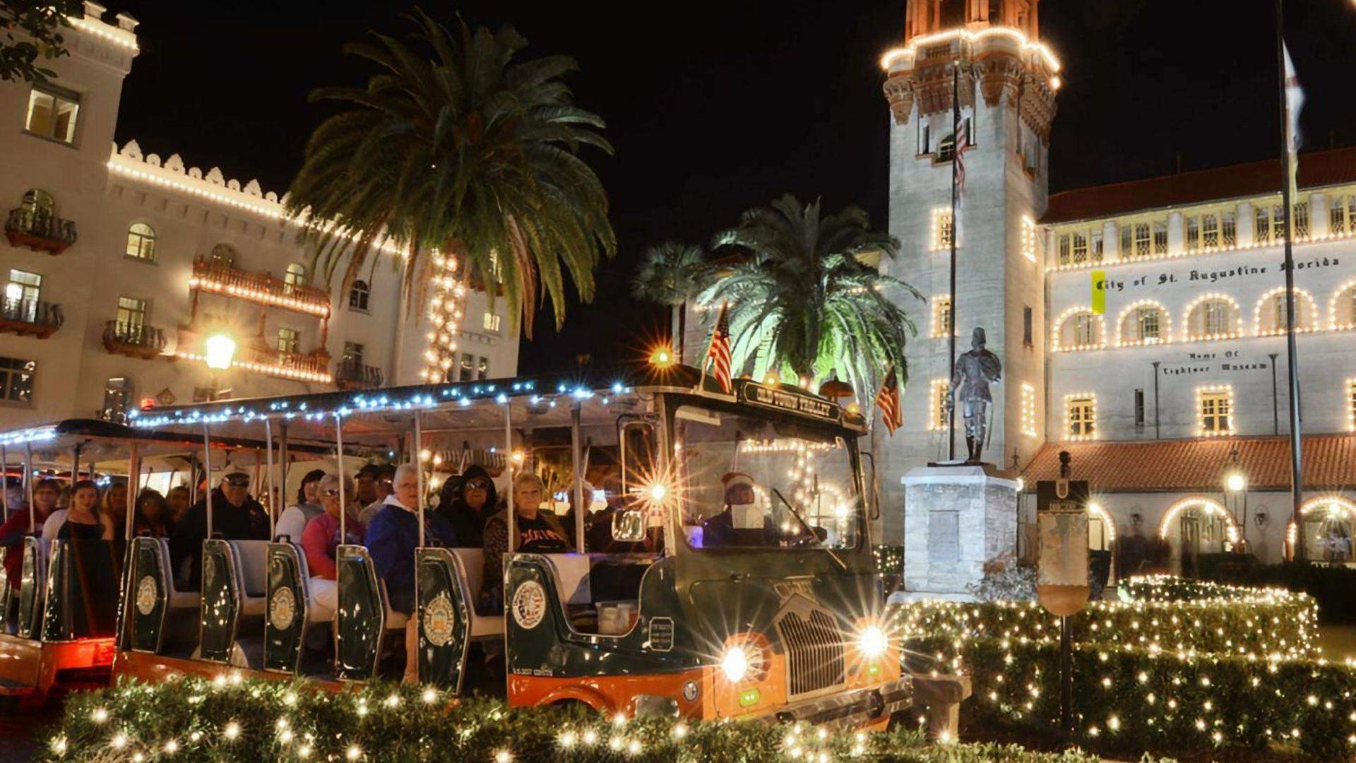 Christmas trolley tour passing Lightner Museum in St. Augustine with white holiday lights, palm trees, and festive nighttime decor