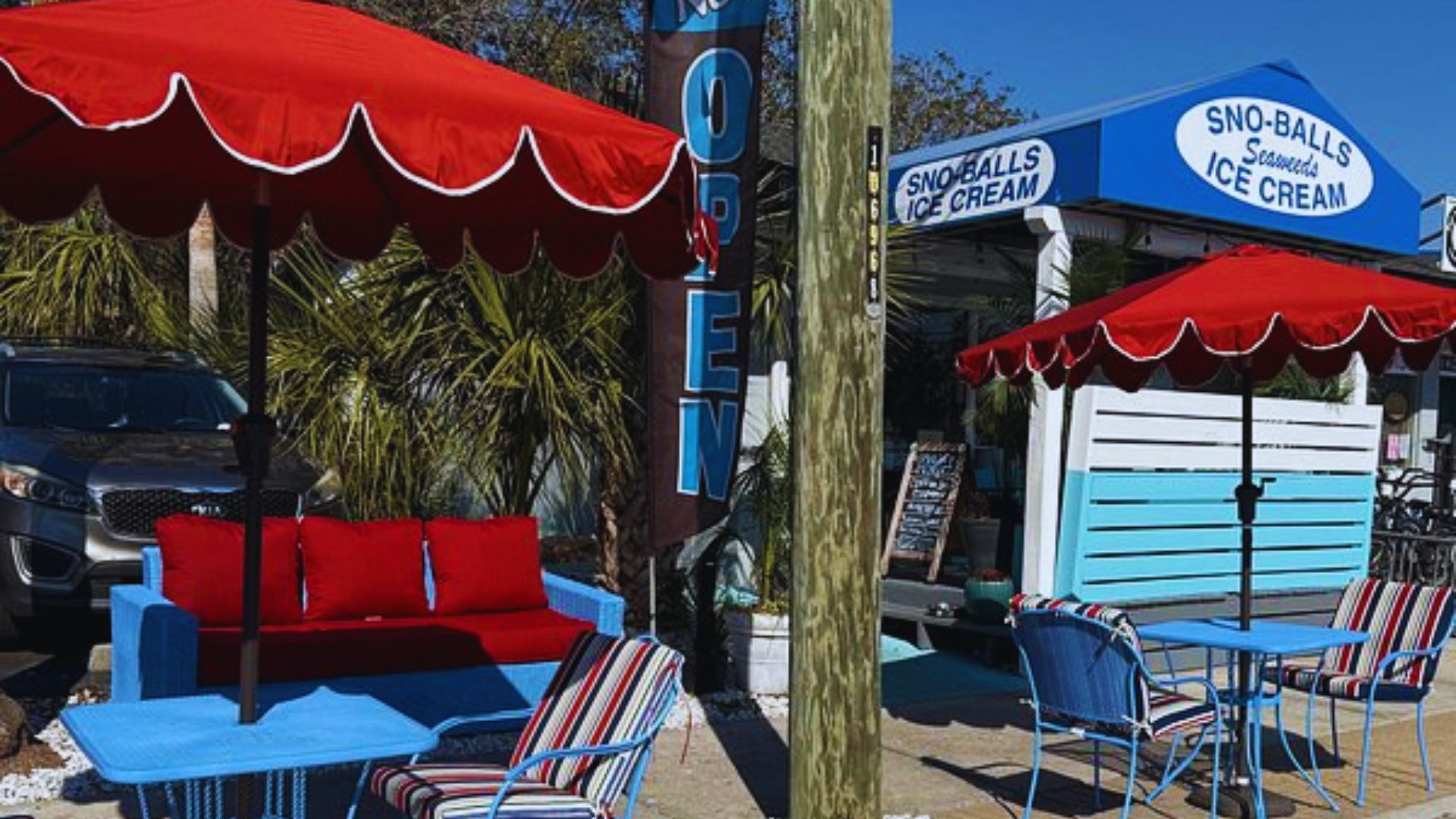 Blue tables and red umbrellas sit outside a Sno Balls ice cream shop on Tybee Island.