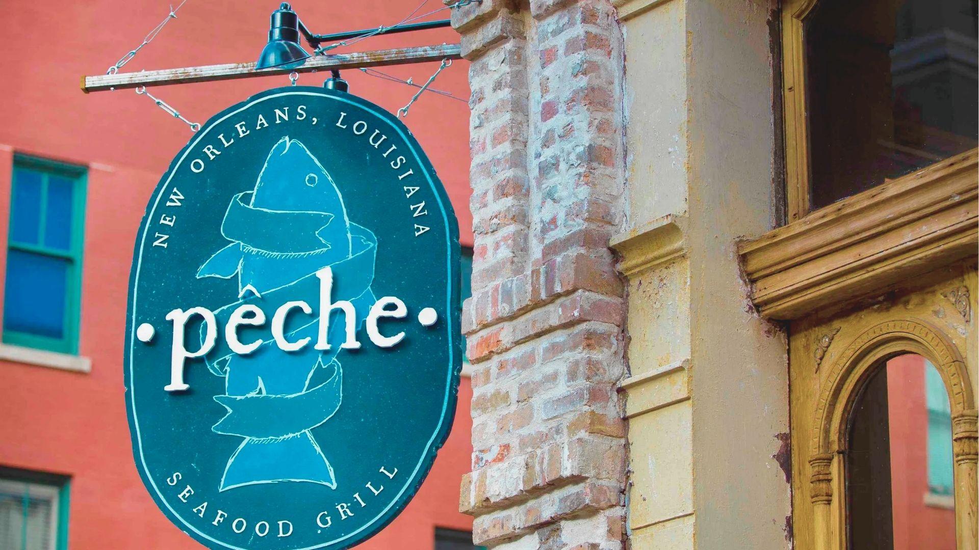 Oval teal “Pêche Seafood Grill” sign with a fish illustration hangs on a brick wall in New Orleans.
