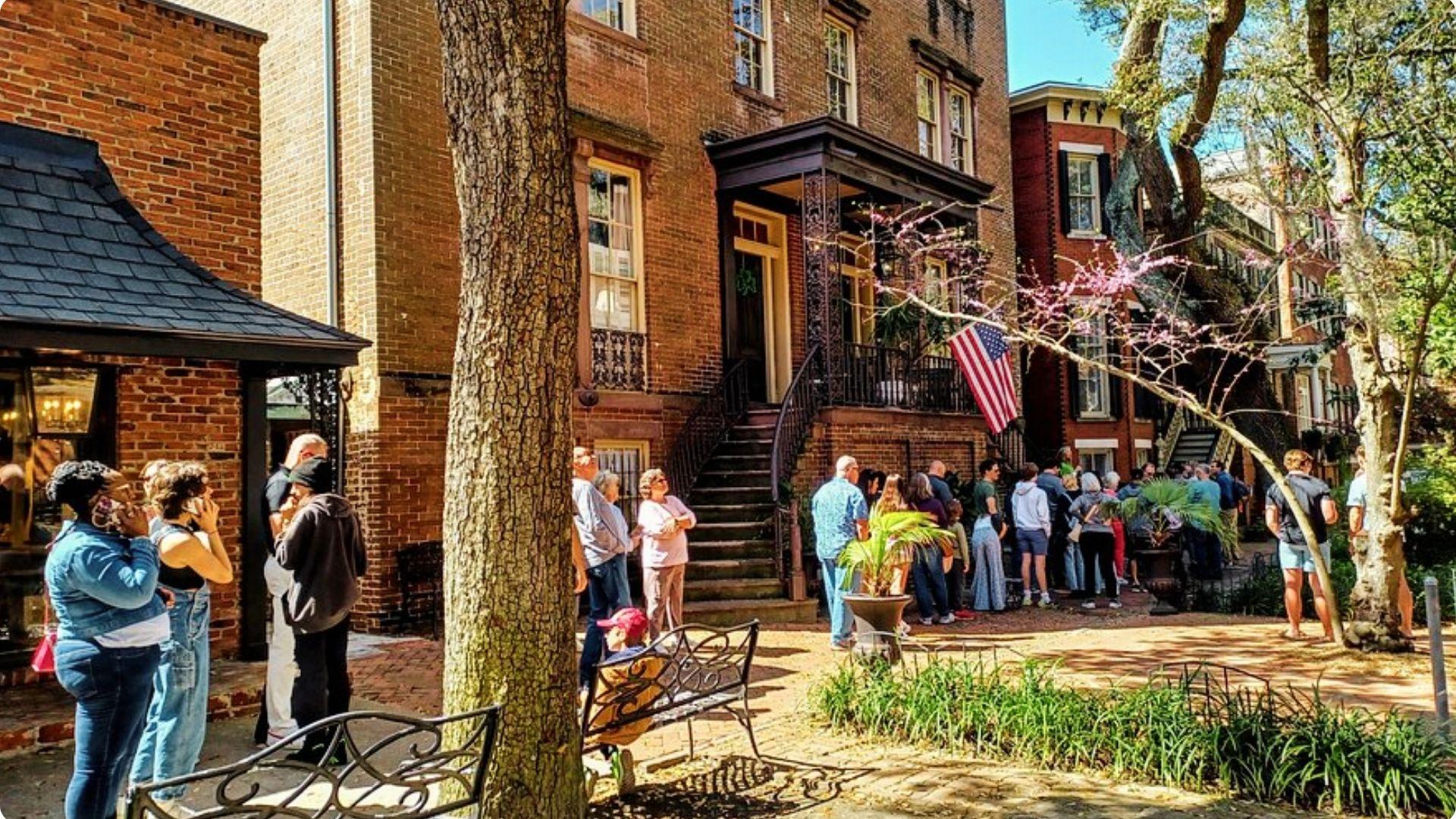 Daytime crowd of guests lining up outside a historic three-story brown brick townhouse.