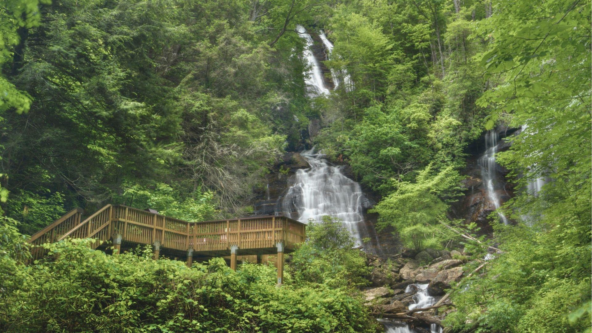 Anna Ruby Falls cascades over rocky cliffs into a stream surrounded by lush green forest.