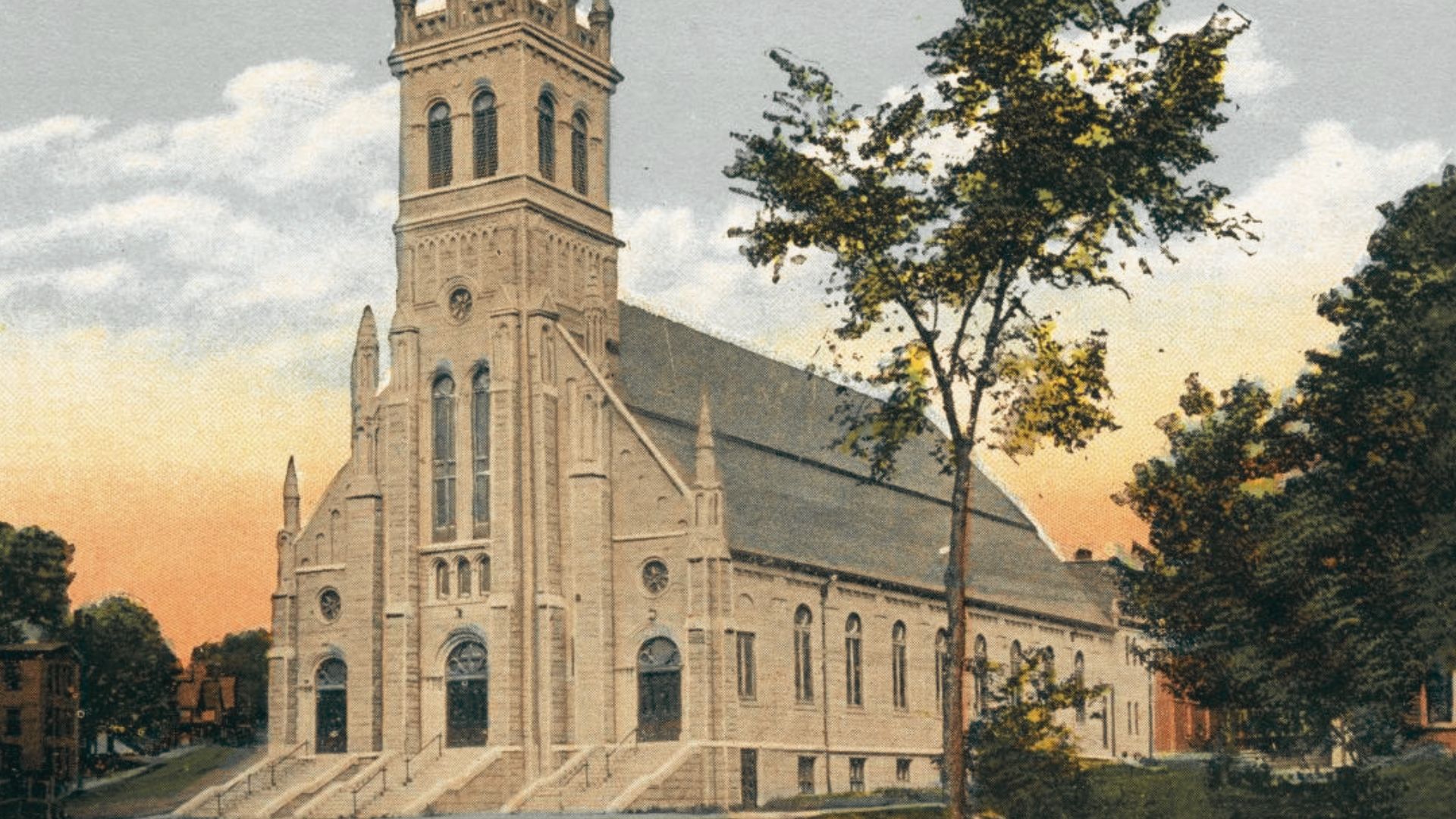 St. Augustine Church with soaring stone tower and grand stairways framed by trees at sunset.