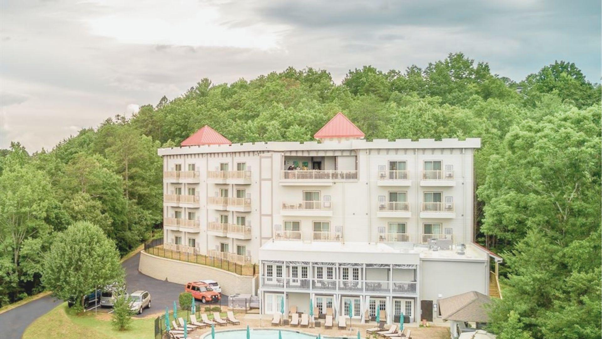 Aerial view of a castle-style hotel with red turret roofs and balconies surrounded by lush green forest in Helen, GA.