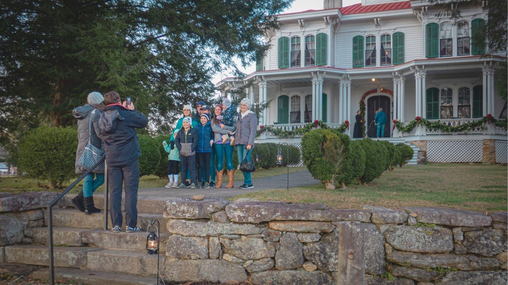 A family poses for a photo on stone steps in front of a Victorian home decorated with holiday garland.