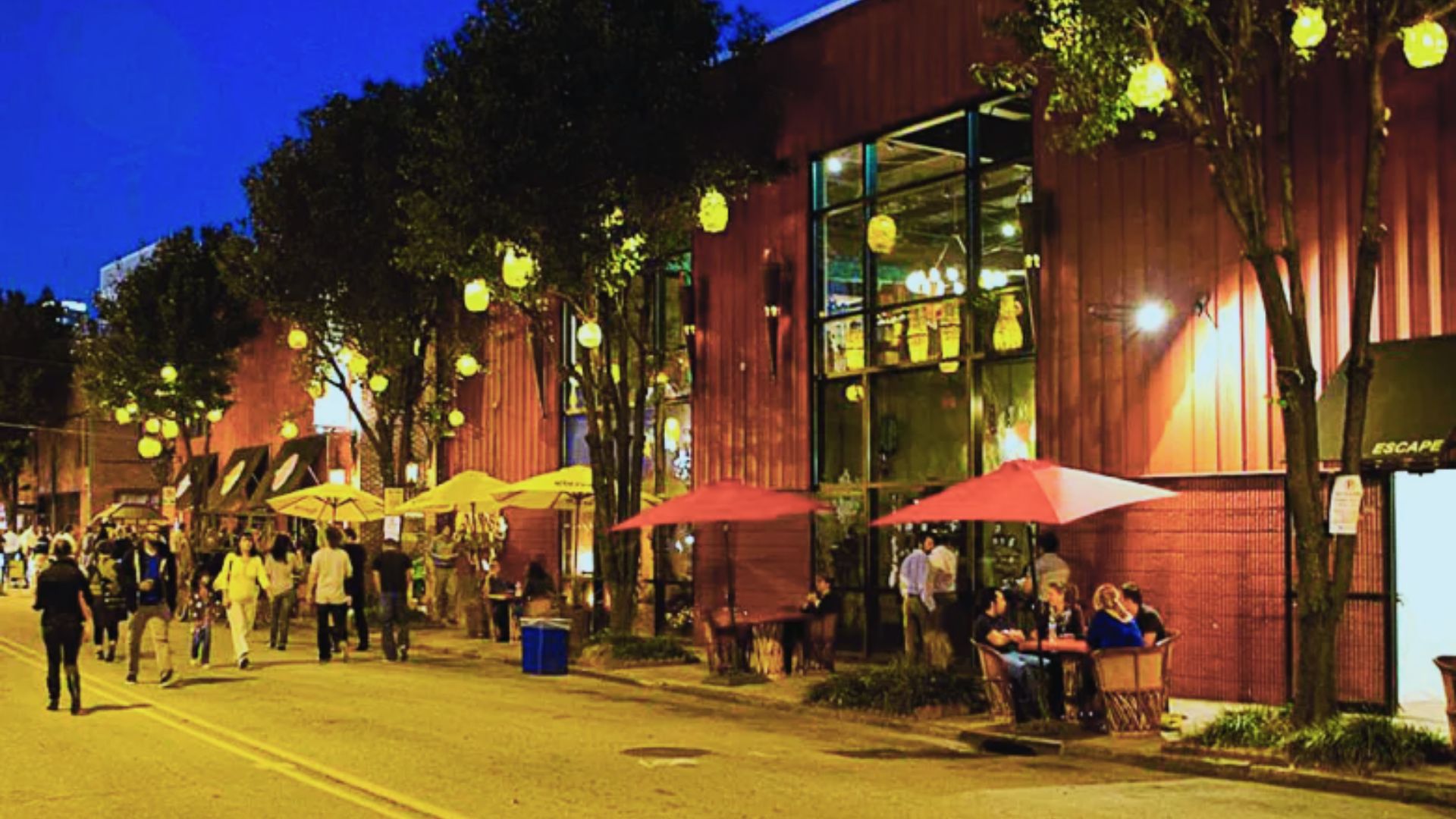 People walk and dine along Castleberry Hill streets under glowing lanterns outside restaurants at night.