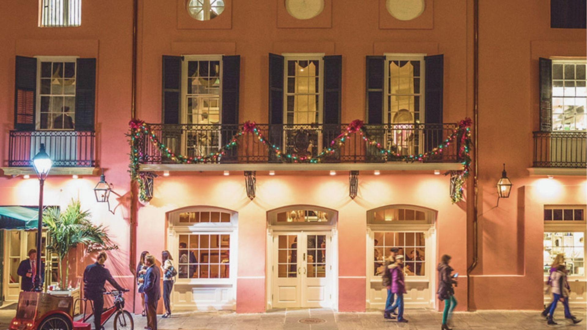 Brennan's pink French Quarter building lit at night, with festive garland draped across its iconic wrought-iron balcony.