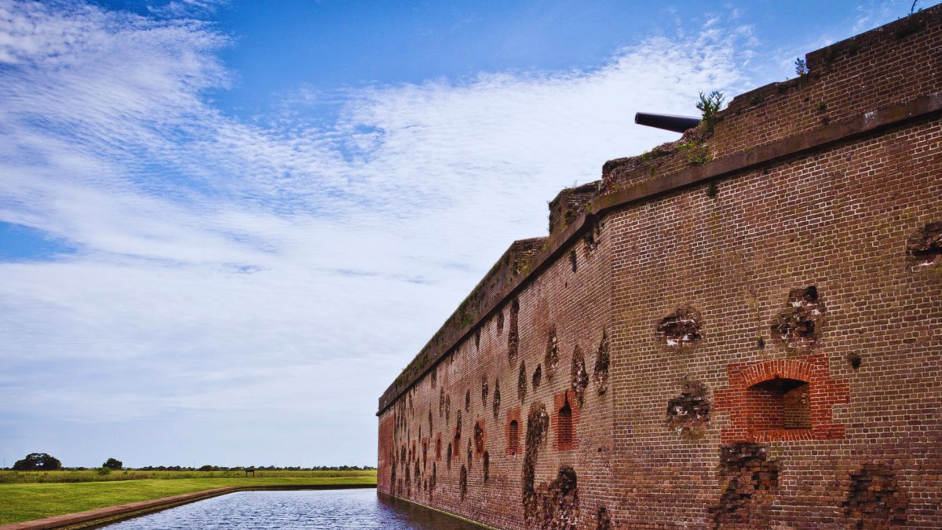 Old brick walls of Fort Pulaski rise beside calm water under a blue sky with clouds.