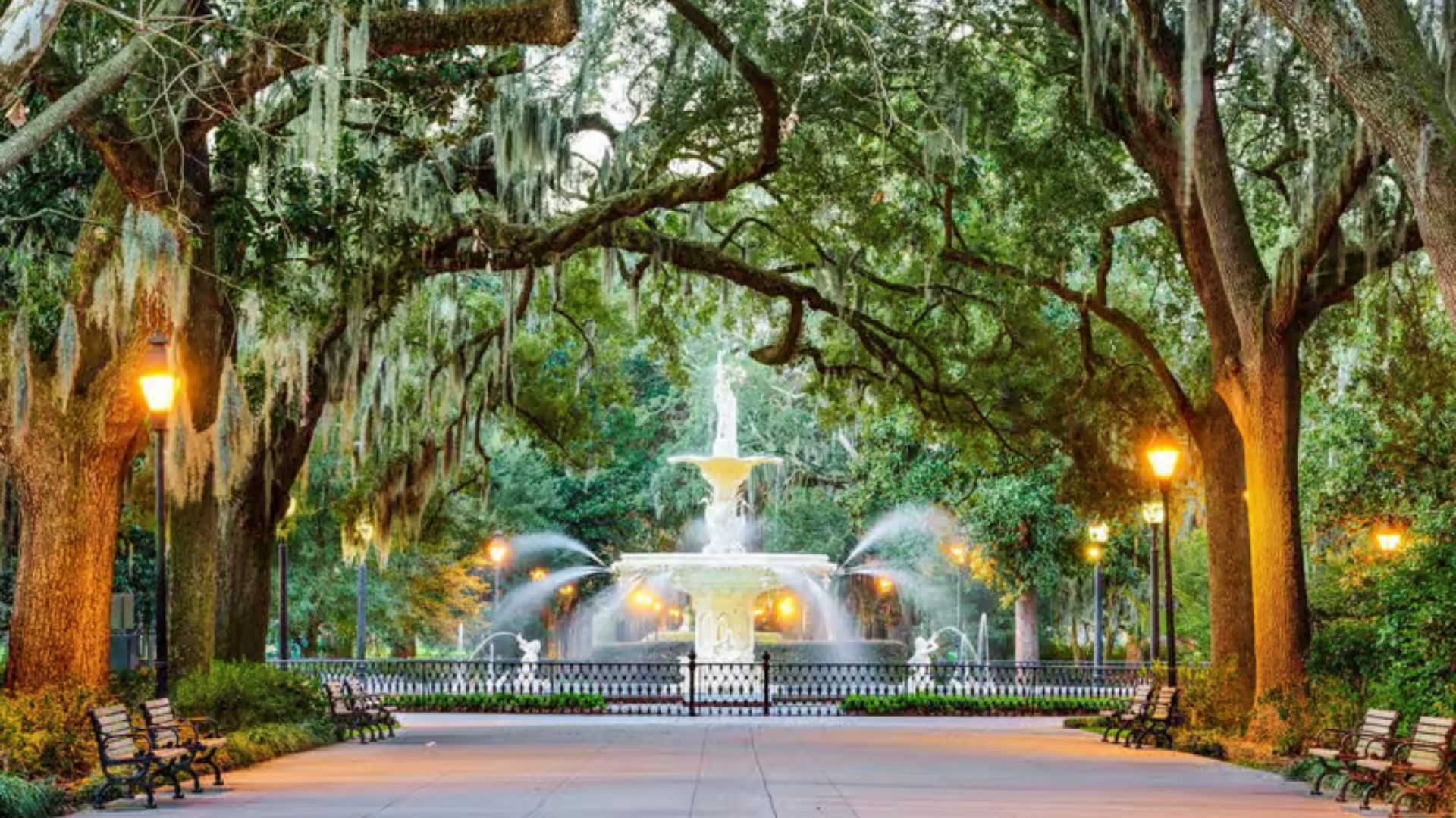 The iconic Forsyth Park fountain surrounded by live oak trees with Spanish moss and lit gas lamps at dusk in Savannah, Georgia