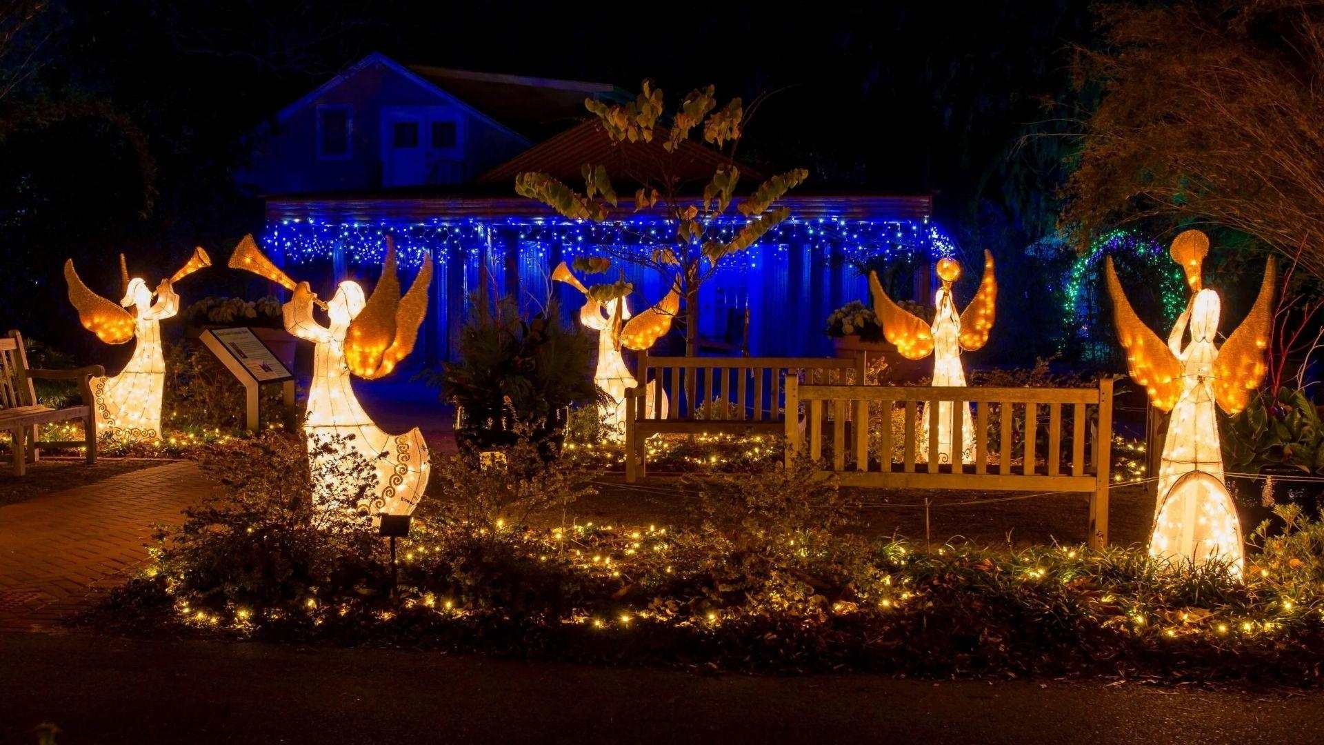 Glowing angel light sculptures with trumpets in Savannah garden, blue Christmas lights on house and pathway at night