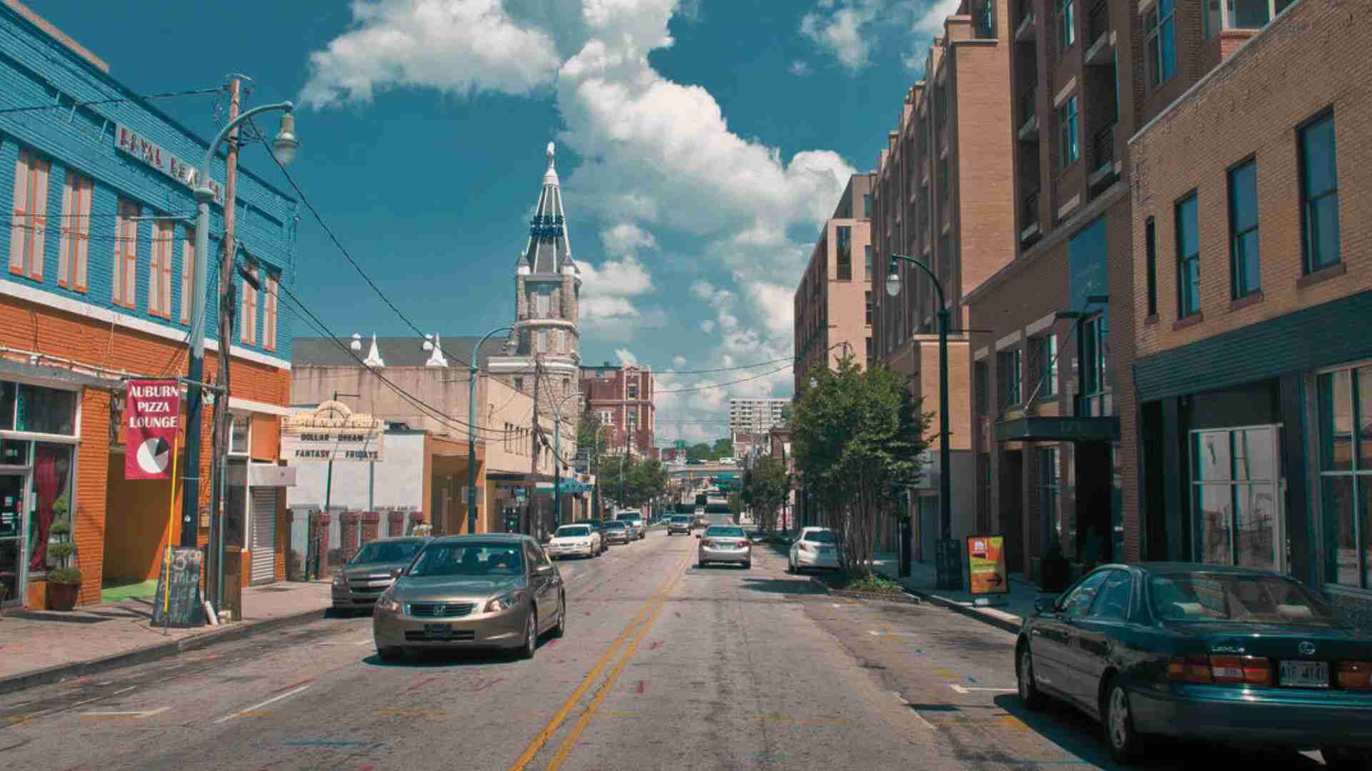 Historic Auburn Avenue street in Atlanta with cars, storefronts, and church steeple under blue skies.