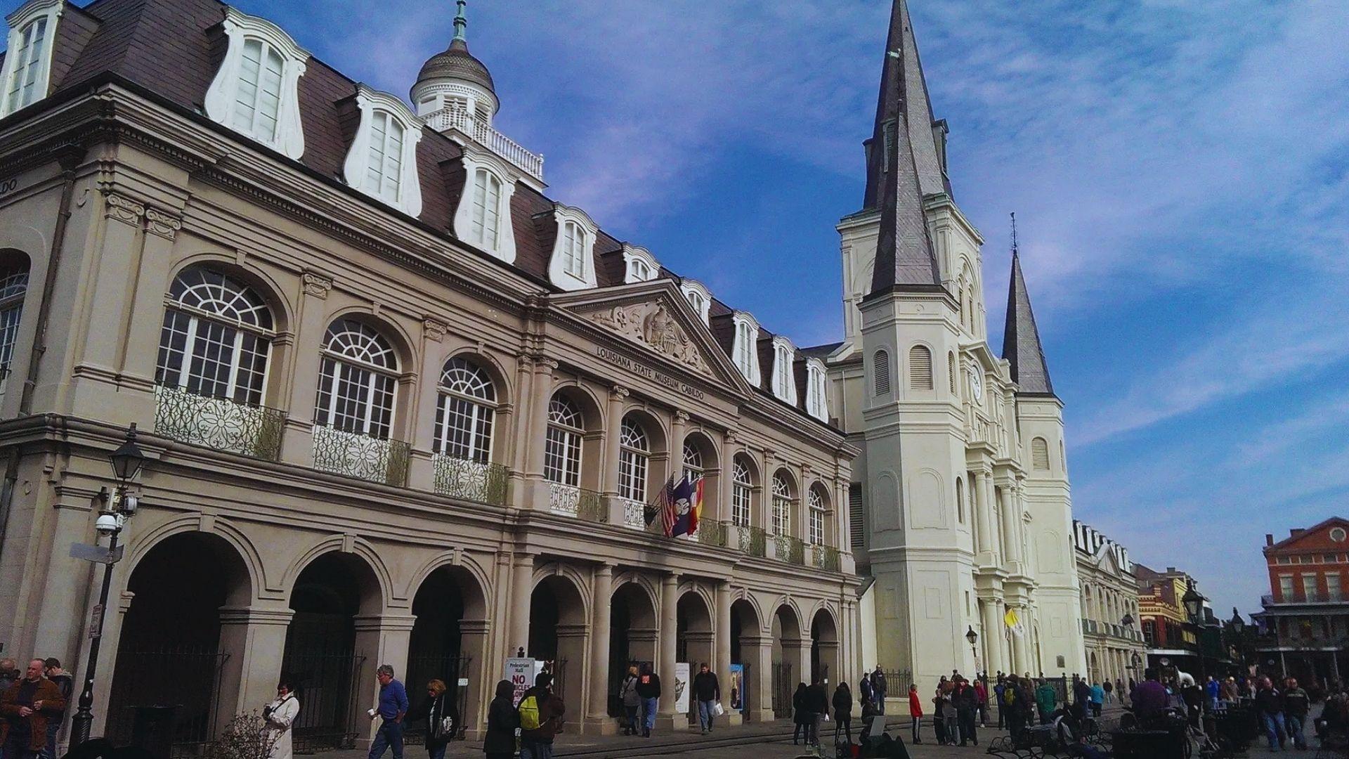 The Cabildo and St. Louis Cathedral in Jackson Square with tourists, flags, arched windows, blue sky, New Orleans