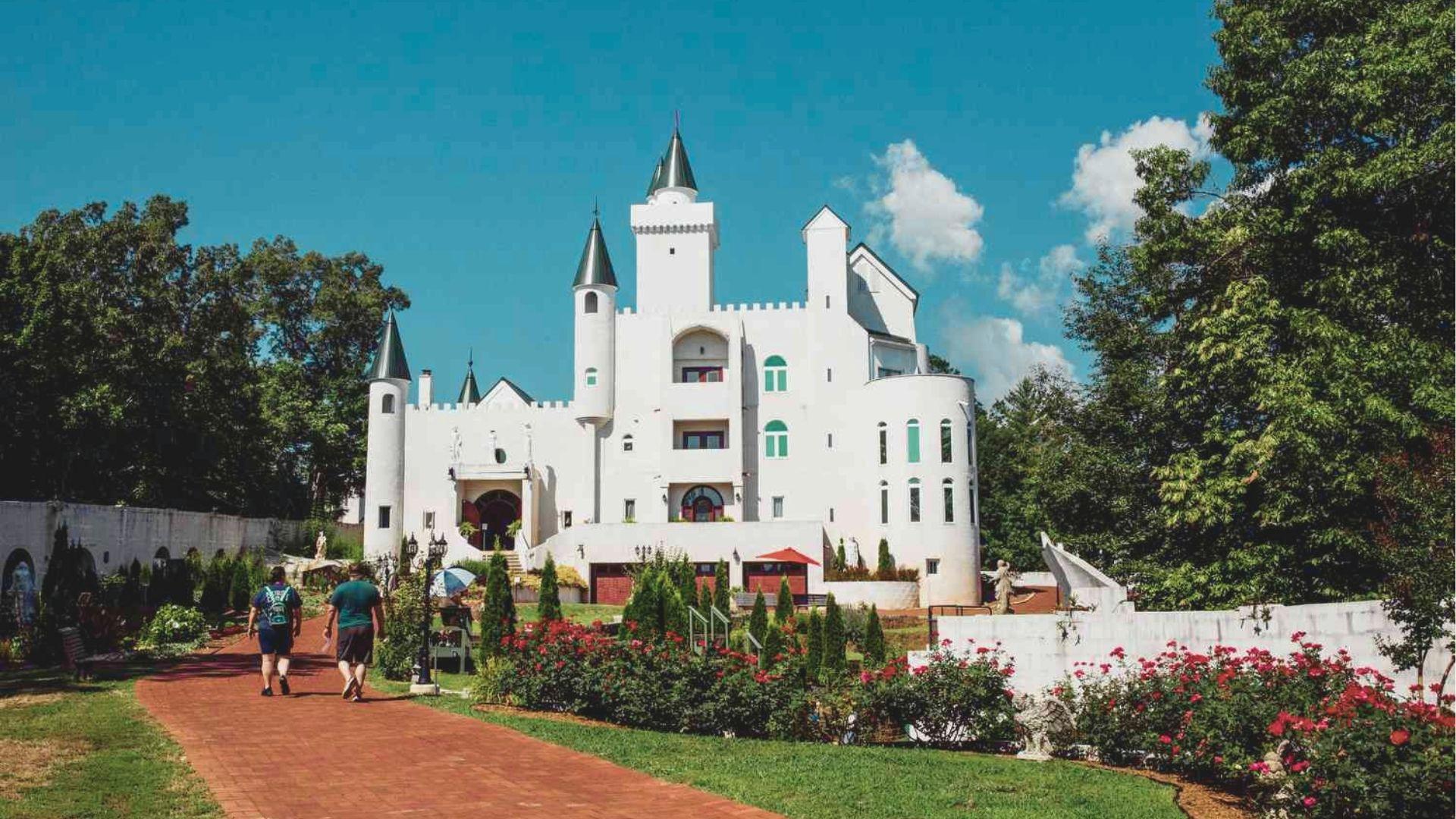 Visitors walk toward Uhuburg Castle on a sunny day along a red brick path lined with rose bushes.