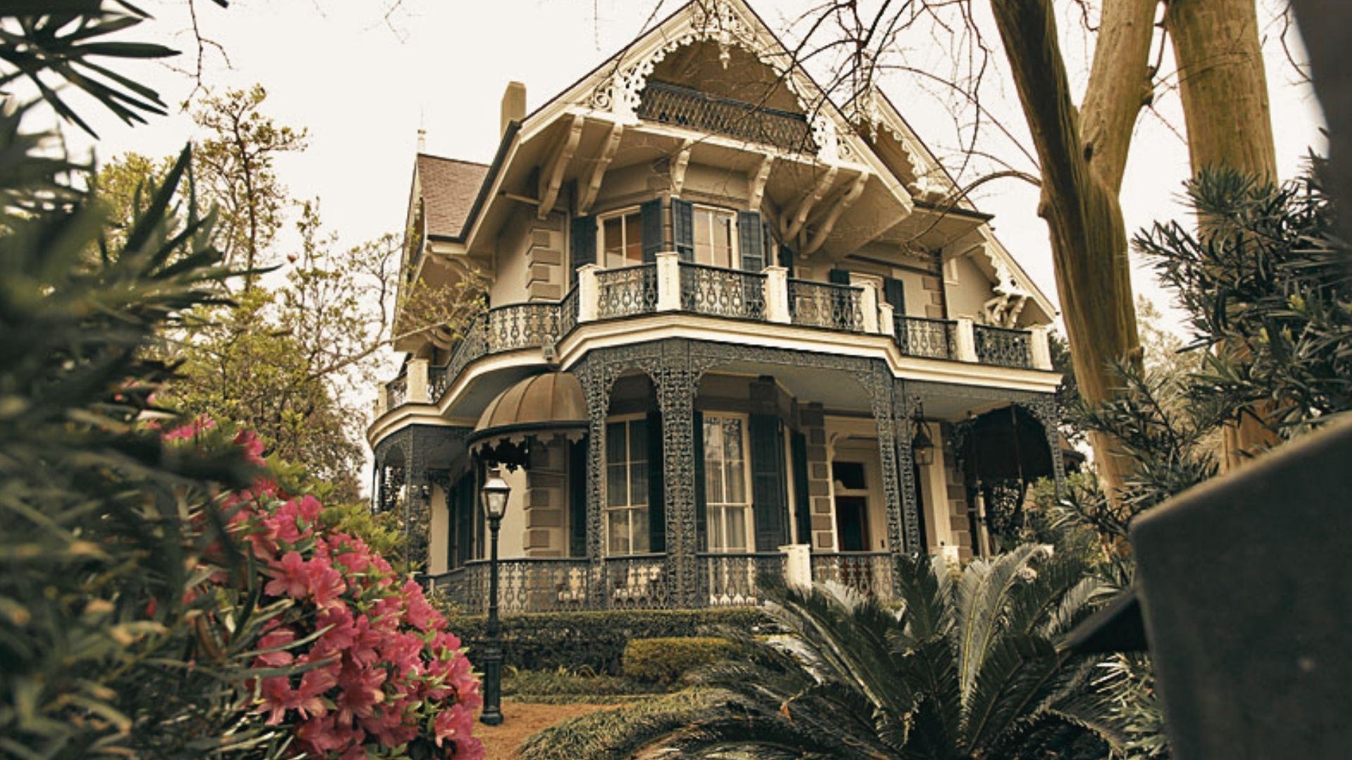 Historic Victorian mansion in Garden District with ornate ironwork balconies, shutters, and lush pink azaleas, sepia-toned photograph