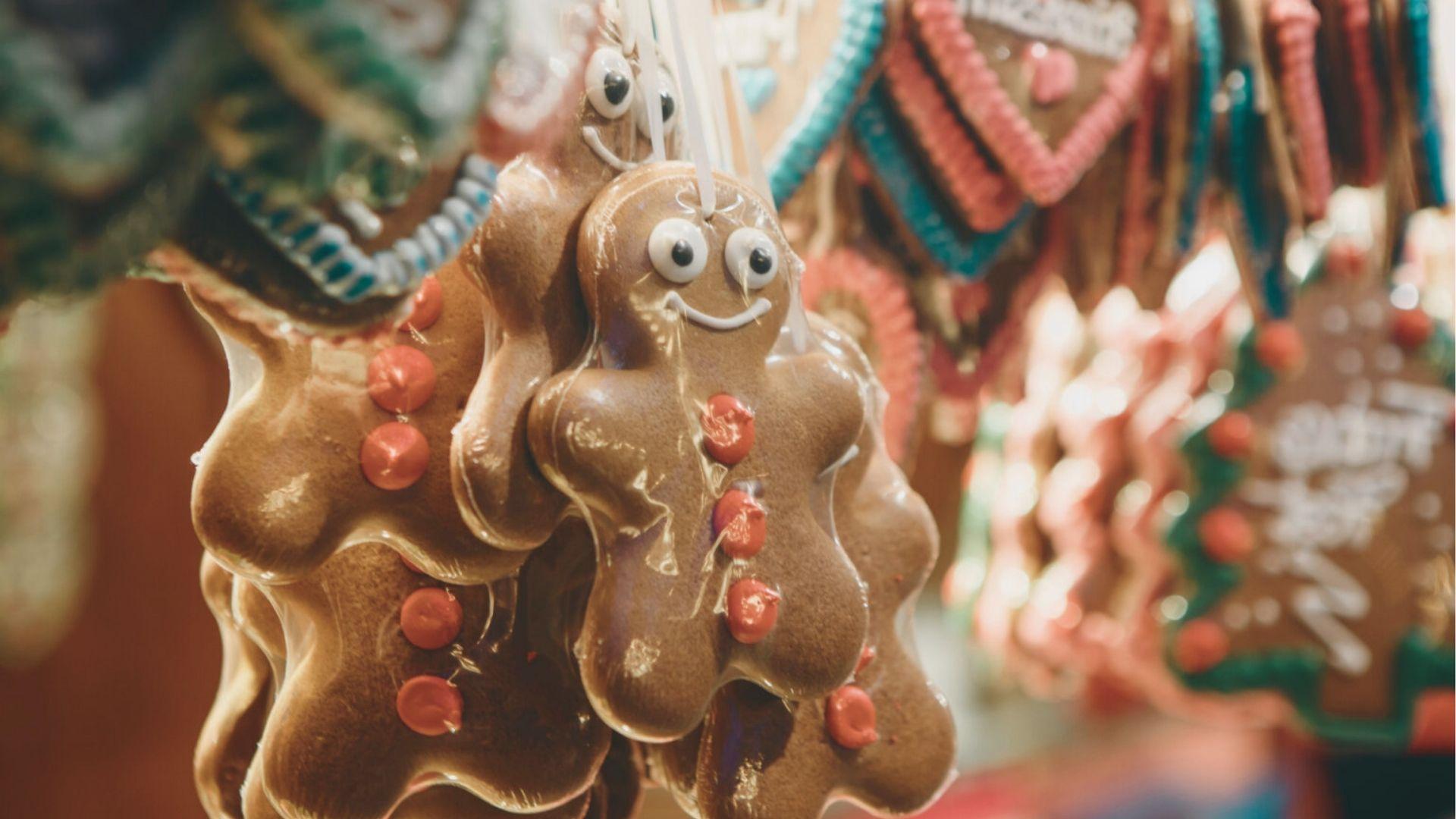 Close-up of smiling gingerbread men cookies with red buttons and googly eyes hanging at a market stall.