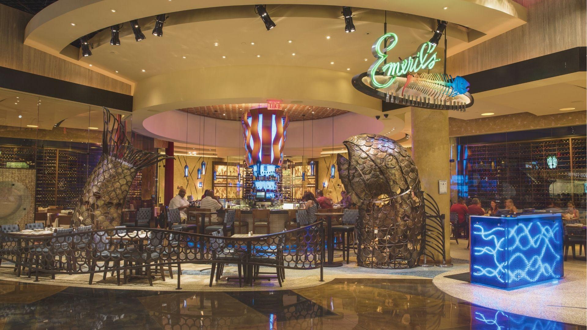 Neon "Emeril's New Orleans" sign glows above sculptural metal fish at the chef-driven fine dining restaurant.