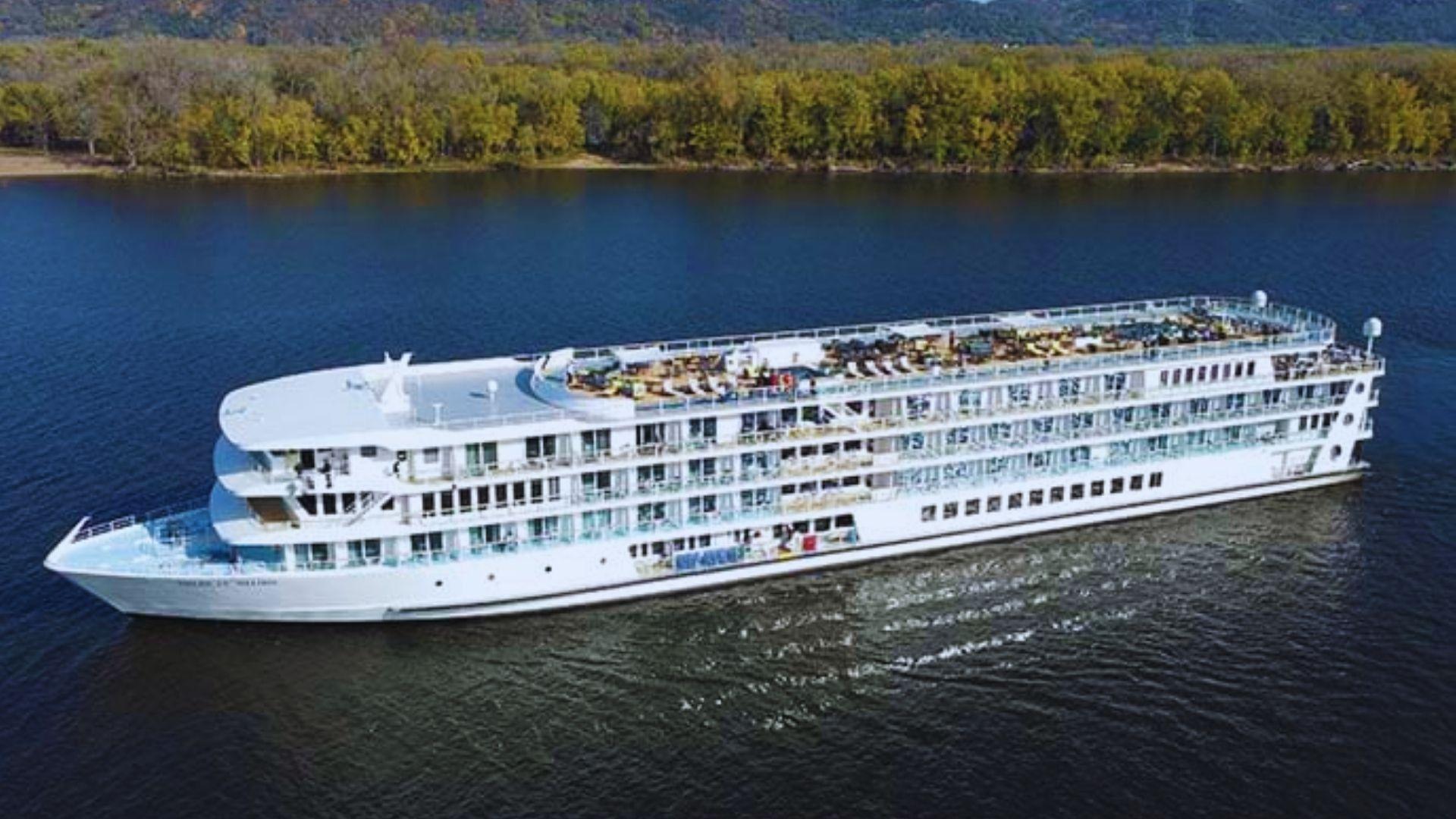 Aerial view of white multi-deck river cruise ship sailing on Mississippi River with forested hills, autumn trees