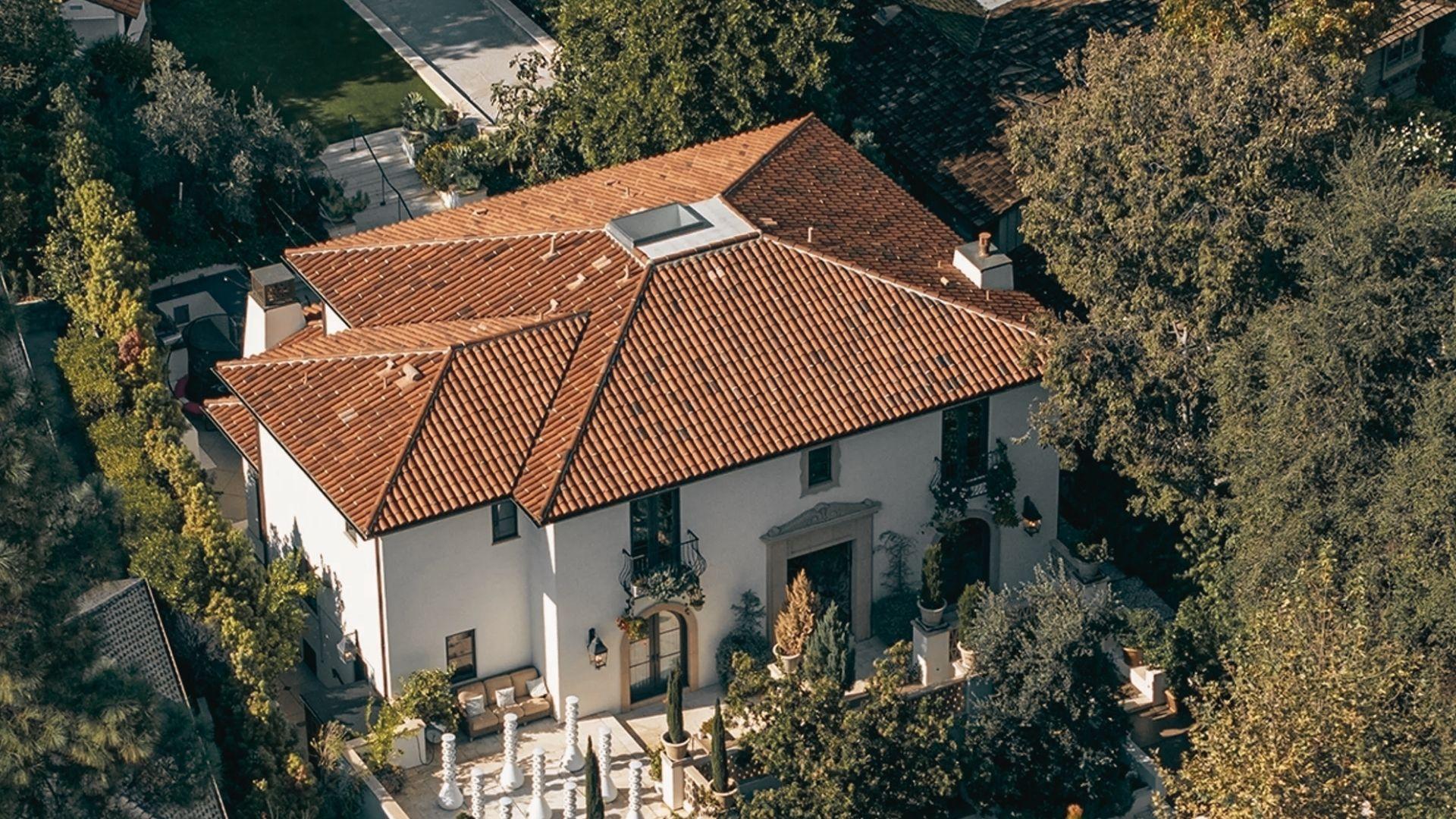 Aerial view of Spanish-style Mediterranean villa with red tile roof, white stucco walls, courtyard, surrounded by trees