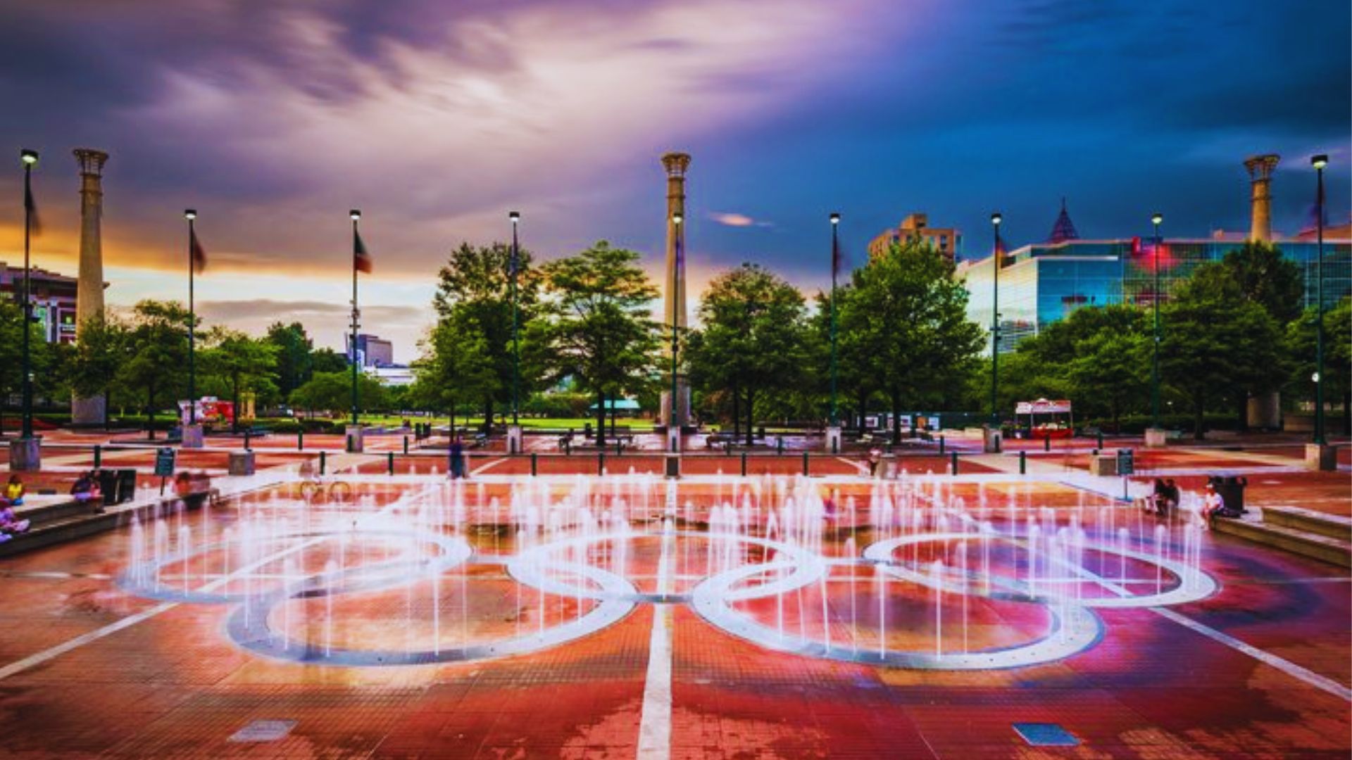 Centennial Olympic Park Fountain of Rings glows at sunset with illuminated water jets and walkways nearby.